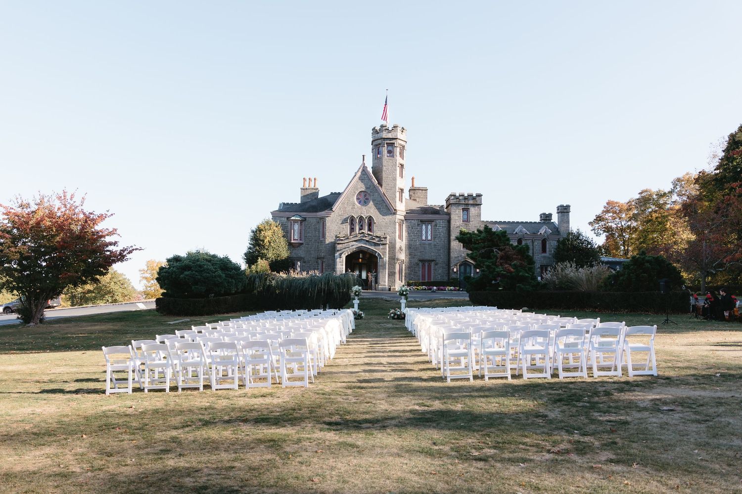 Rows of white chairs set up for an outdoor wedding ceremony on a hilltop with a stone building in the background.