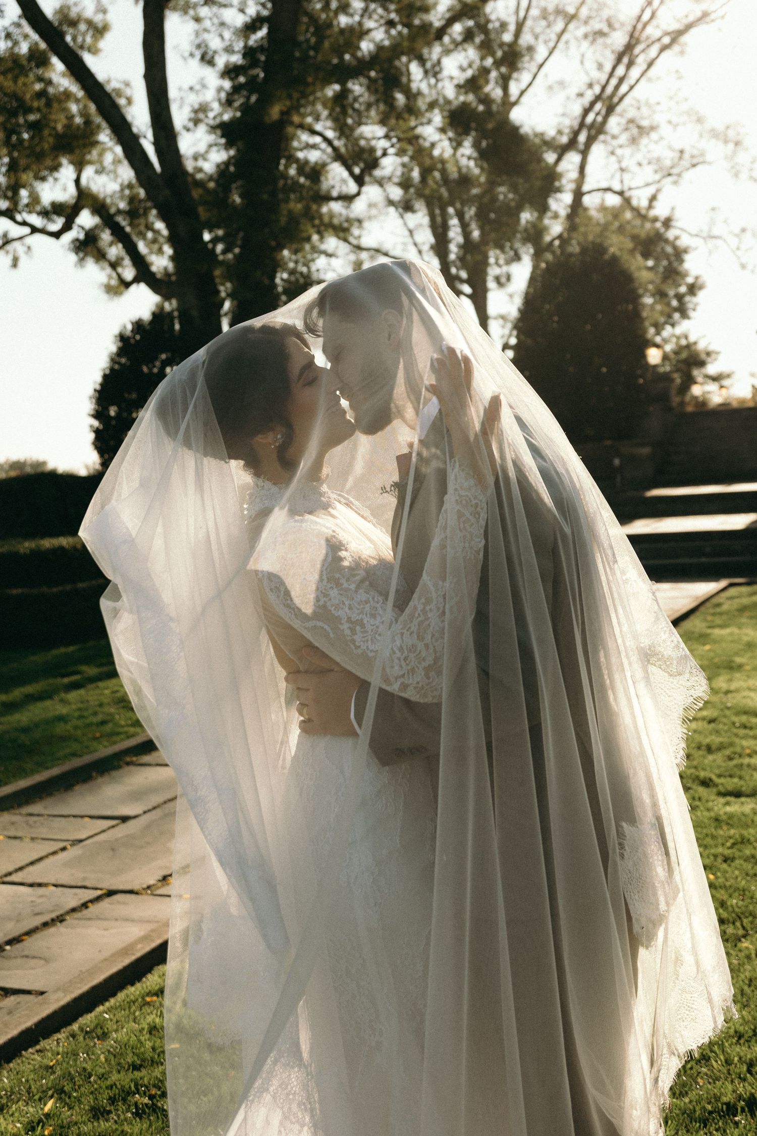 Ethereal white wedding dress with flowing tulle veil photographed in golden sunlight against a natural outdoor setting.