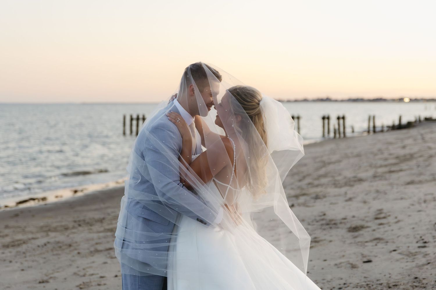 A romantic couple shares tender moments on a sandy beach at sunset with ocean waves in the background.
