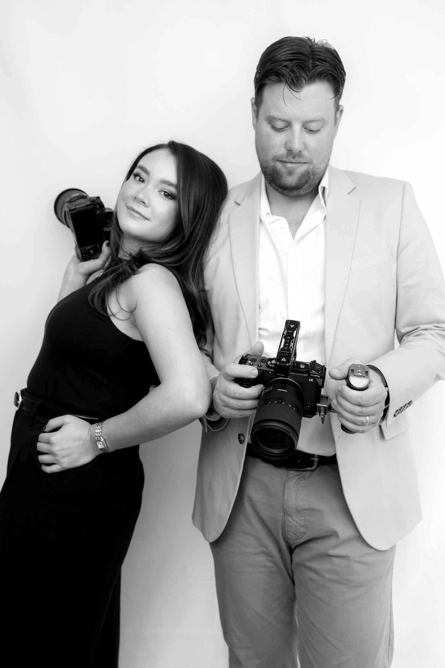 A series of four black and white photos showing photographers examining and holding their cameras in different poses.