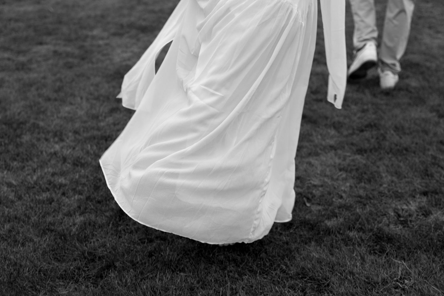 A couple in wedding attire dances on a grassy lawn at sunset, their white dress flowing in graceful movement.