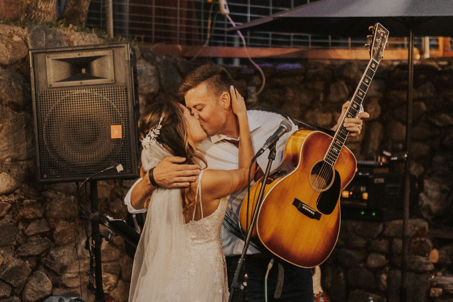 A couple embraces at sunset with an acoustic guitar and speaker visible in an outdoor setting.