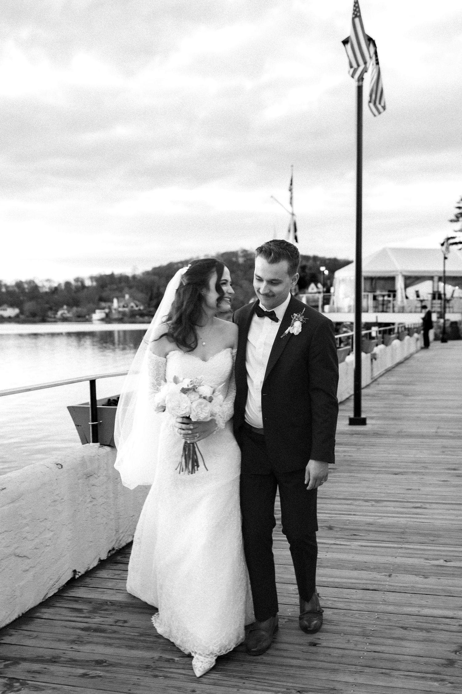 A romantic wedding couple shares intimate moments while walking along a wooden pier by the ocean.