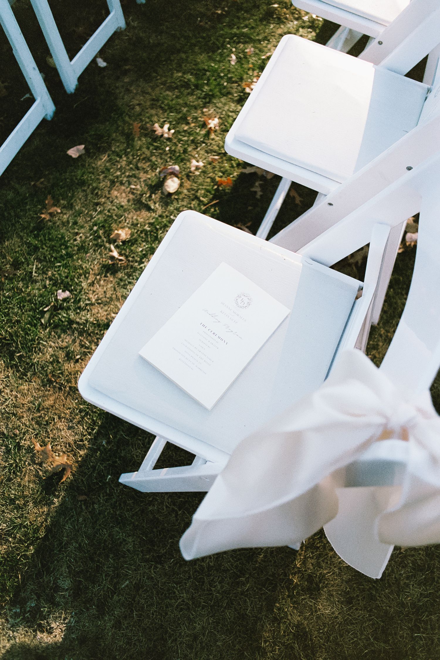 White wooden folding chairs arranged on grass for an outdoor event or wedding ceremony.