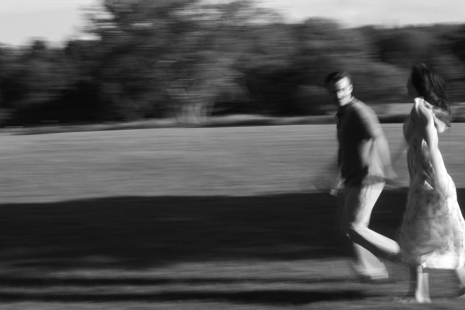 Black and white motion blur photograph of a couple running together across a field.