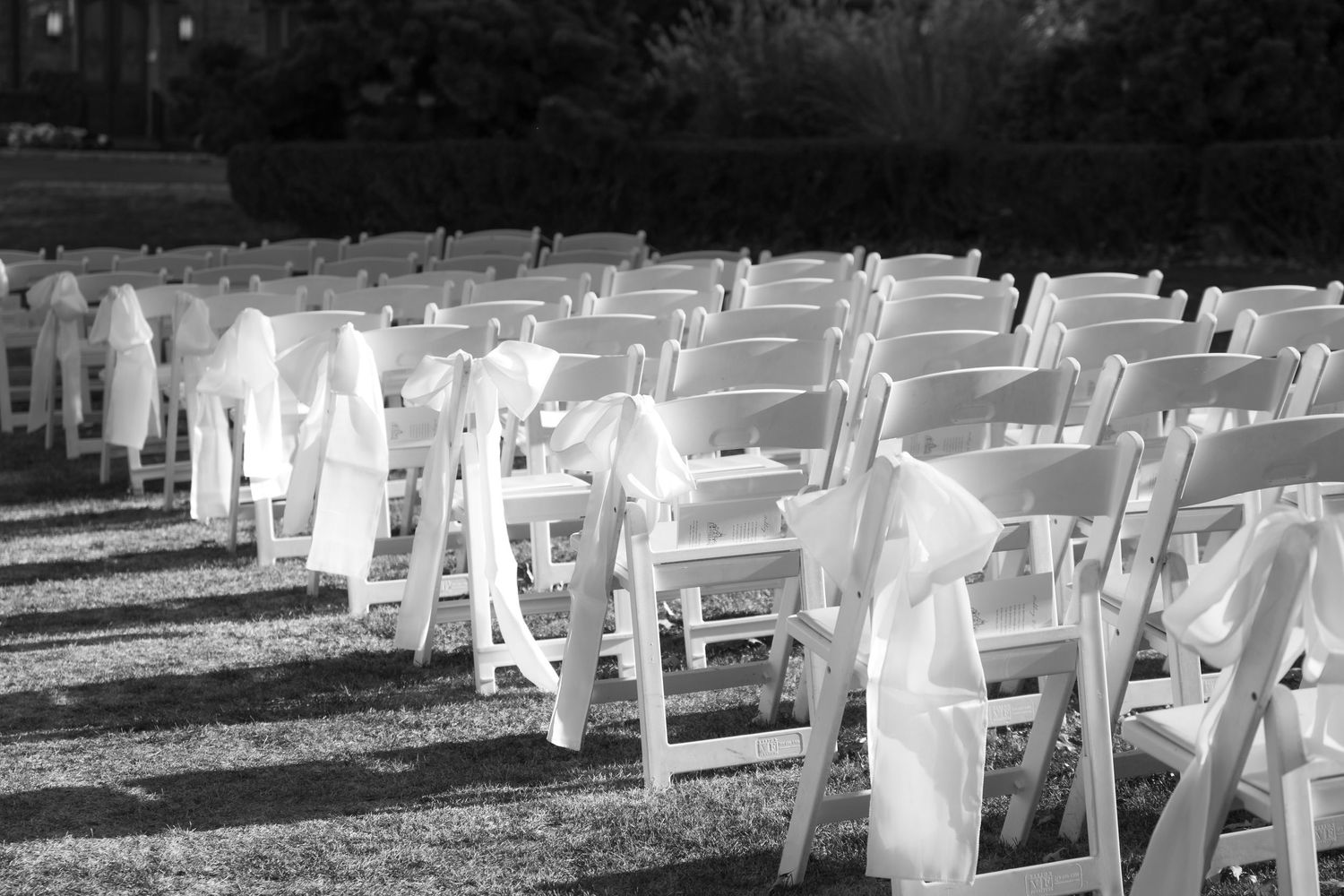 White folding chairs with organza bows arranged in rows for an outdoor wedding ceremony.