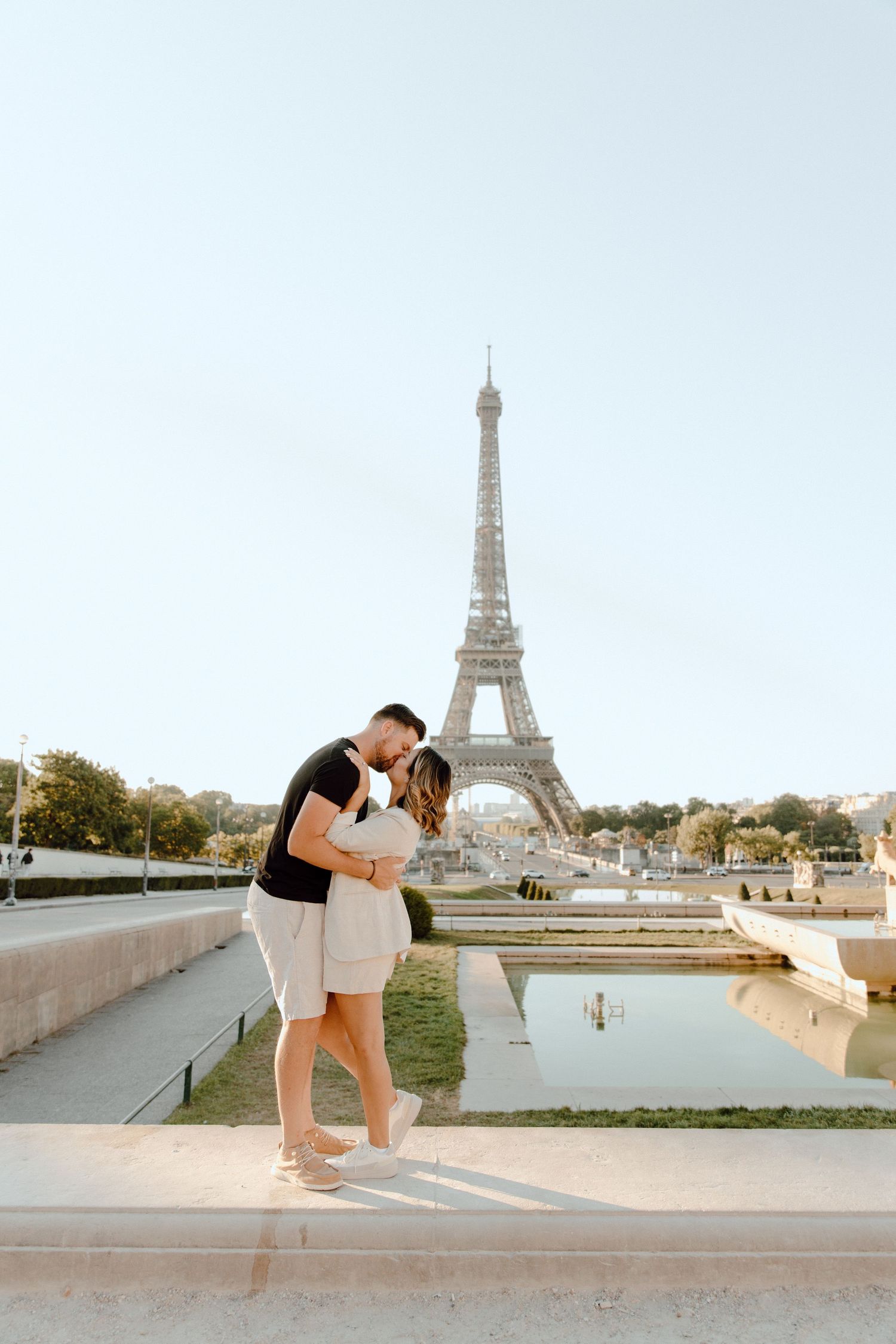 A romantic couple embraces and kisses at Trocadero with the iconic Eiffel Tower visible in the background in Paris.