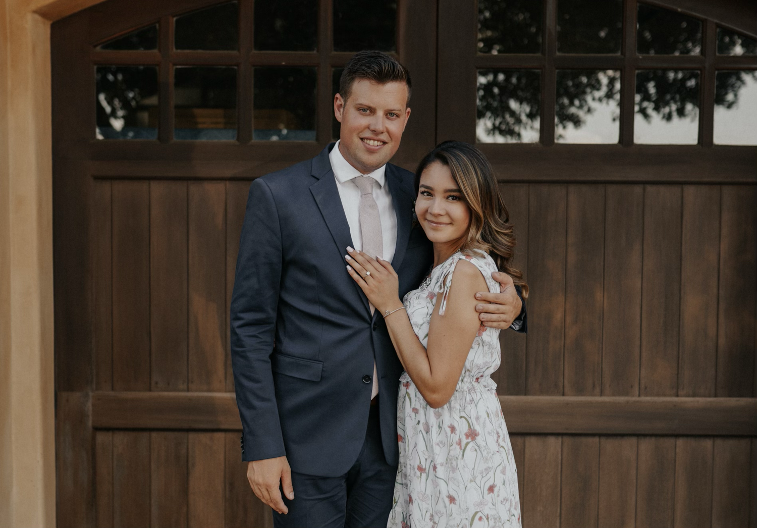 A couple in wedding attire shares a romantic moment in front of a rustic wooden barn door.