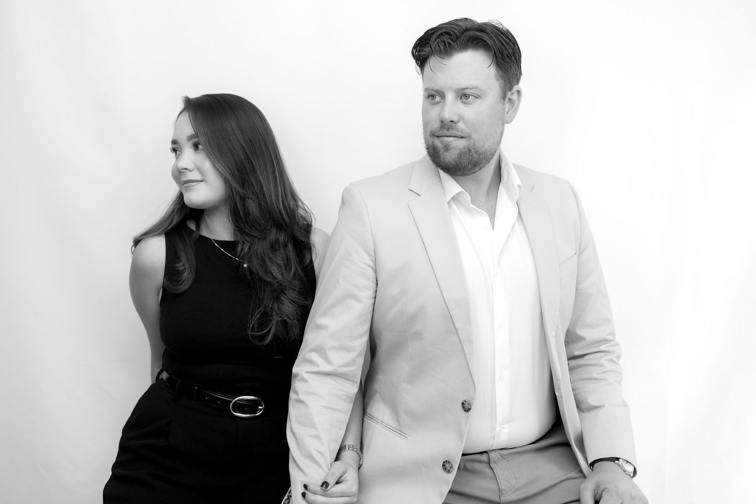 Two people in business attire stand against a white wall during a professional photo session.