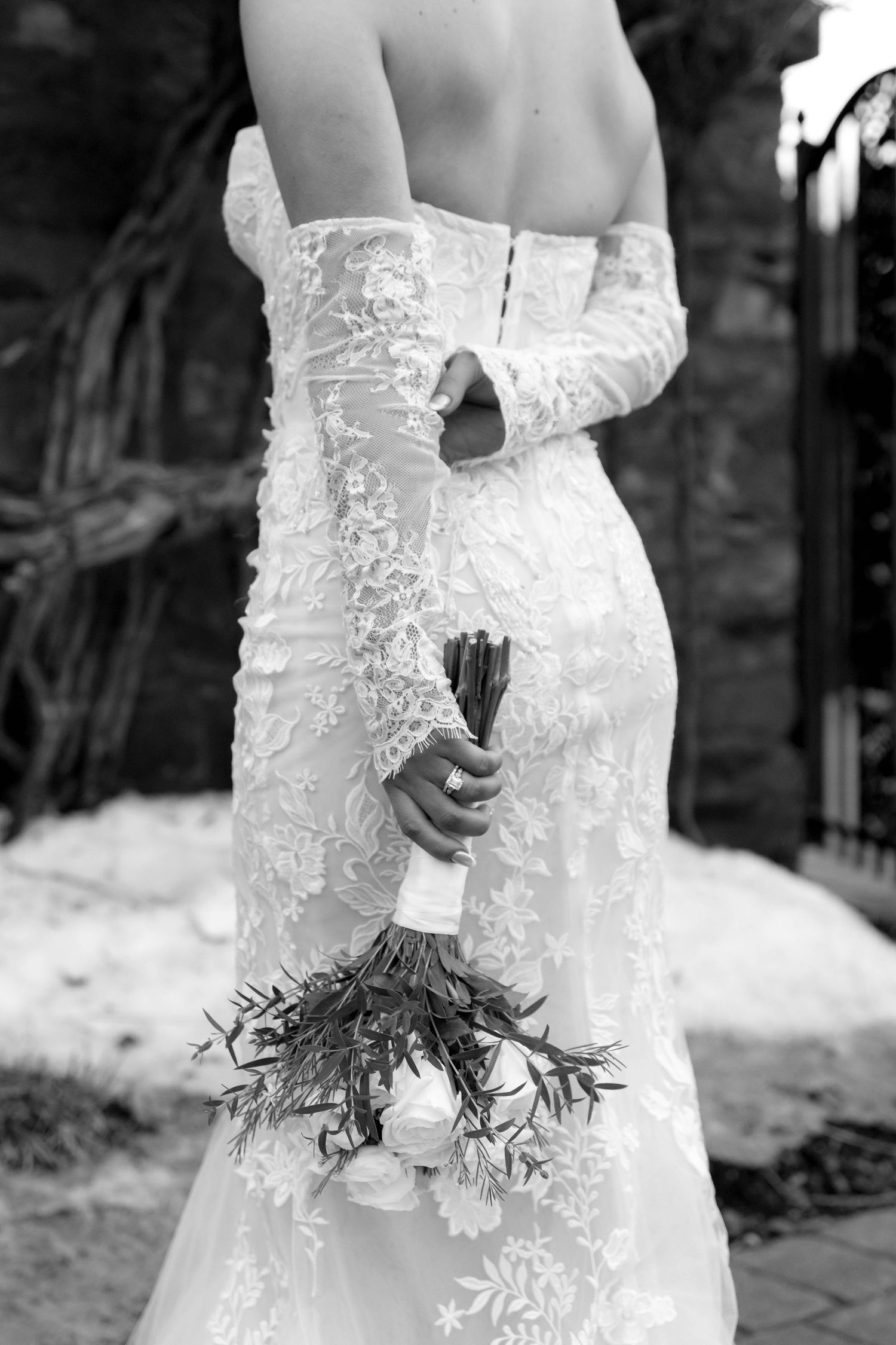 Close-up of an elegant lace wedding dress with a delicate bouquet held behind the back.