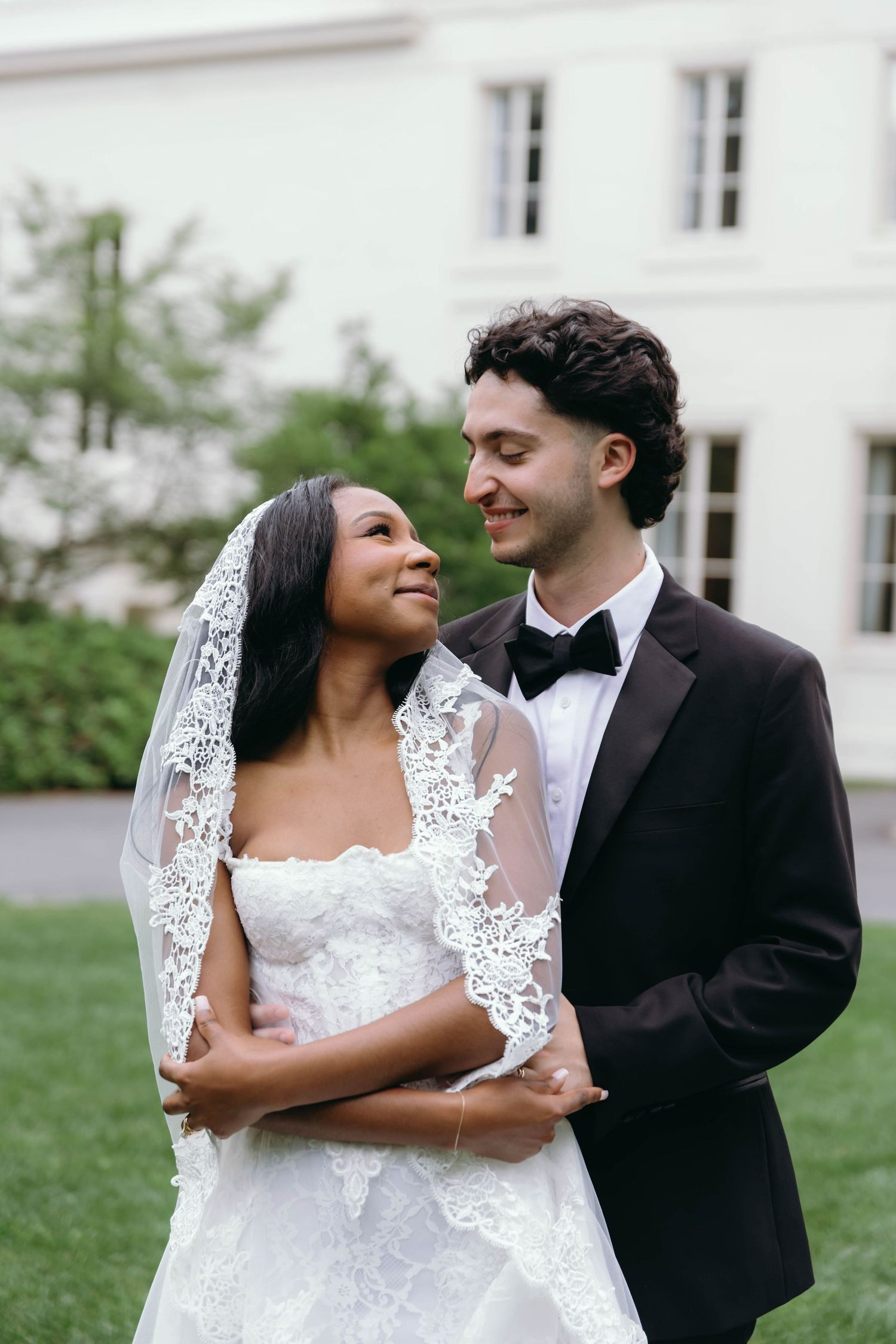 Joyful newlyweds share intimate moments in a series of romantic outdoor wedding portraits against a white building.