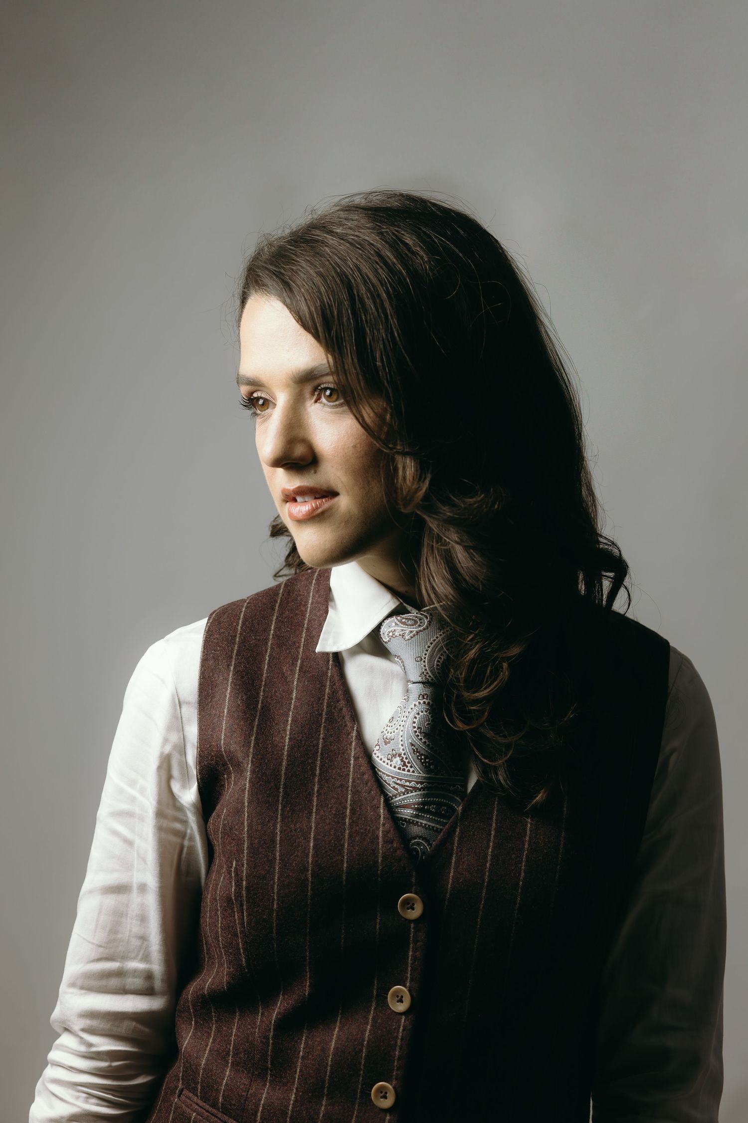 A series of artistic portrait shots showing a person in a brown vest and white shirt against a gray background.