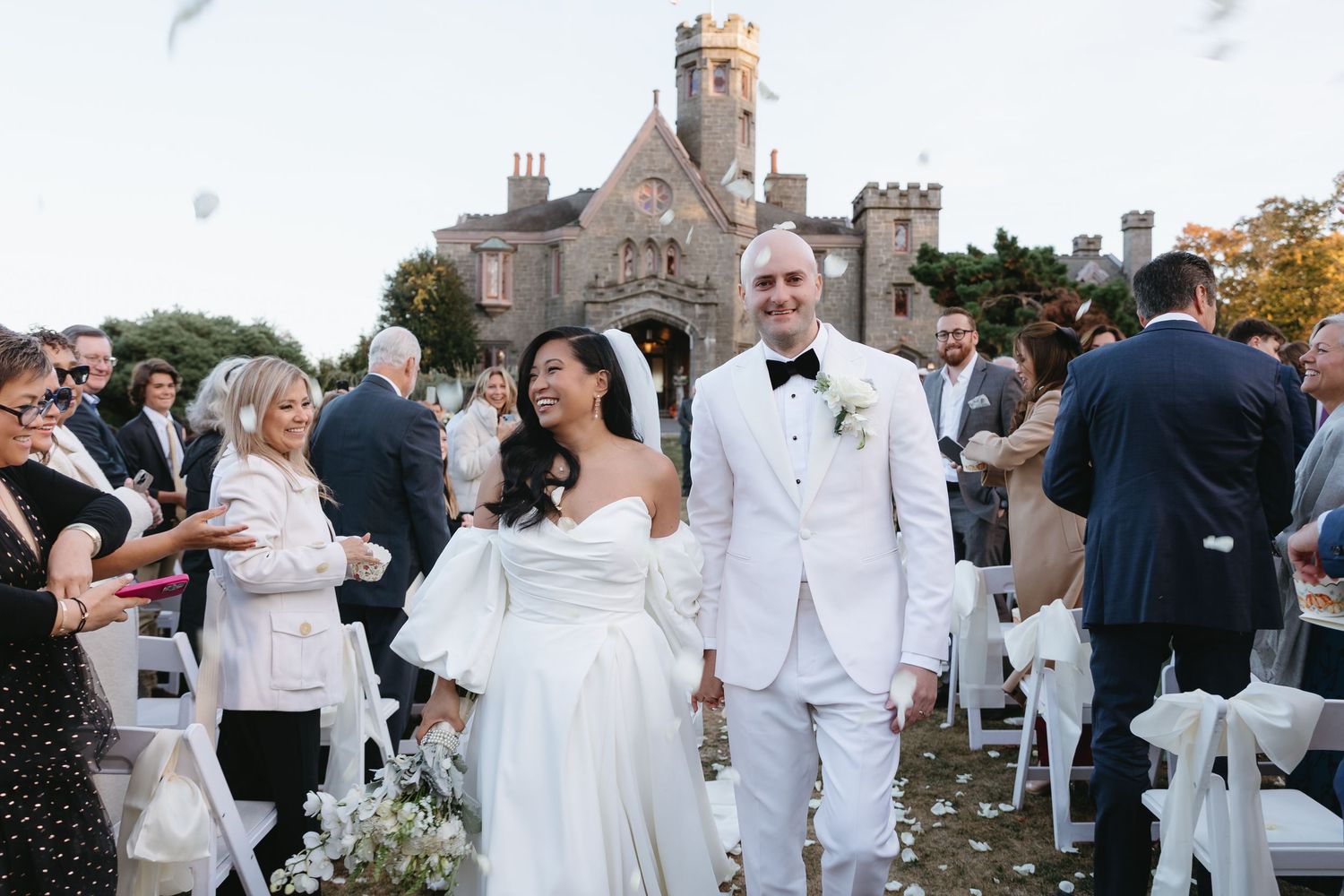 A group of wedding guests in white attire gather on a stone patio for an elegant outdoor celebration.