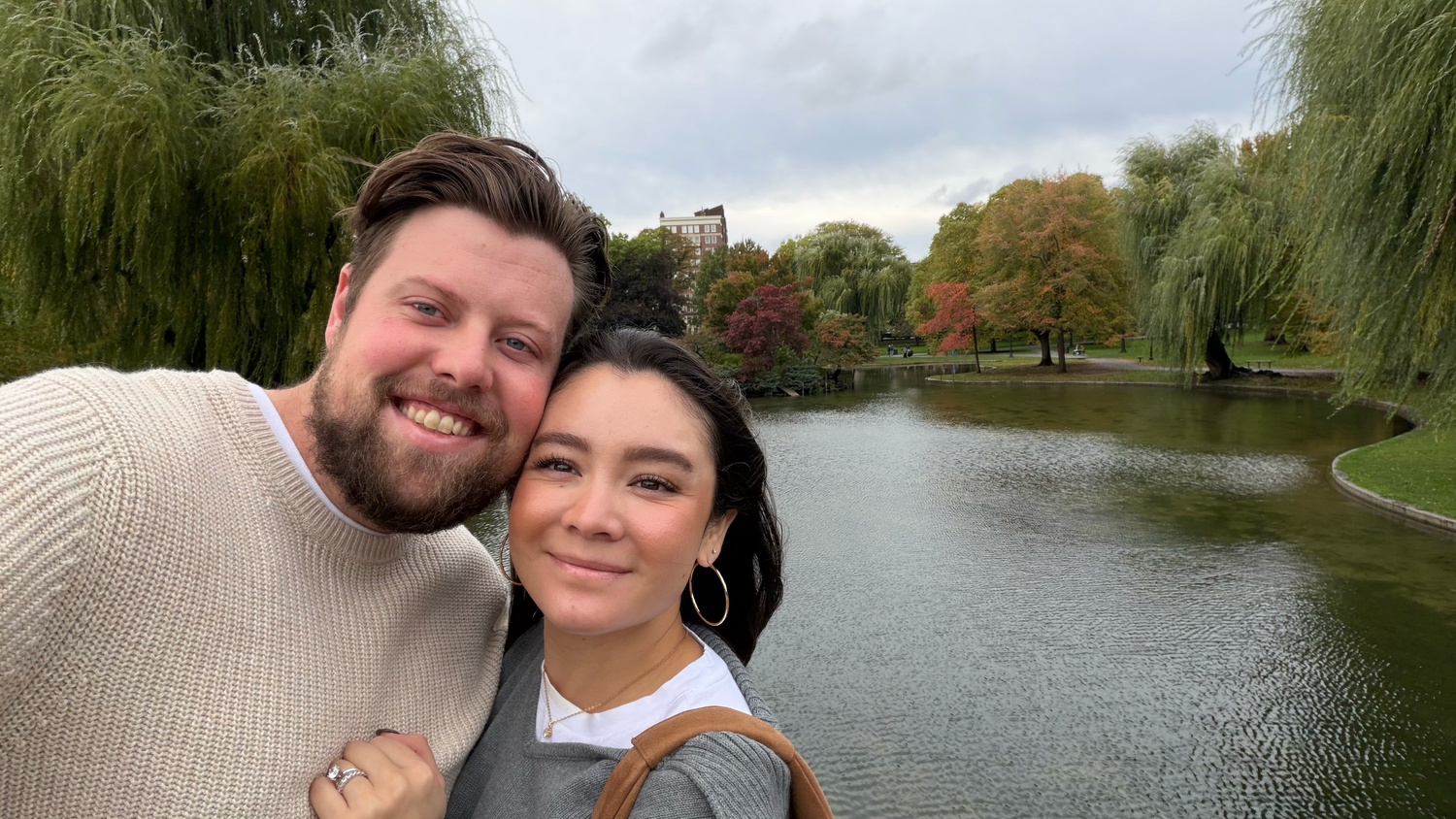 A couple takes a series of selfies by a scenic lake surrounded by autumn trees and foliage.