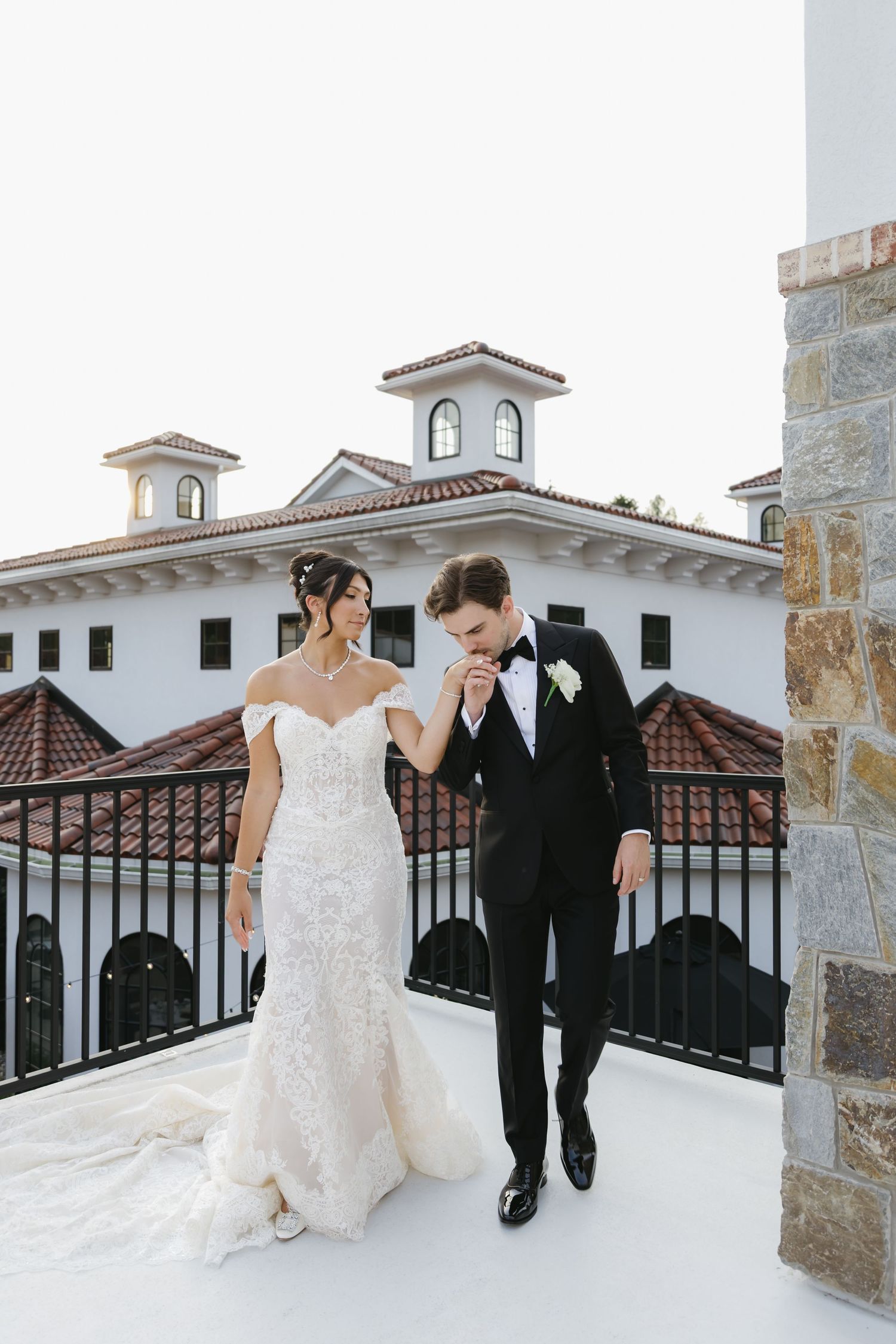 A romantic couple sits together on a white stone ledge during their wedding at an elegant Mediterranean-style venue.