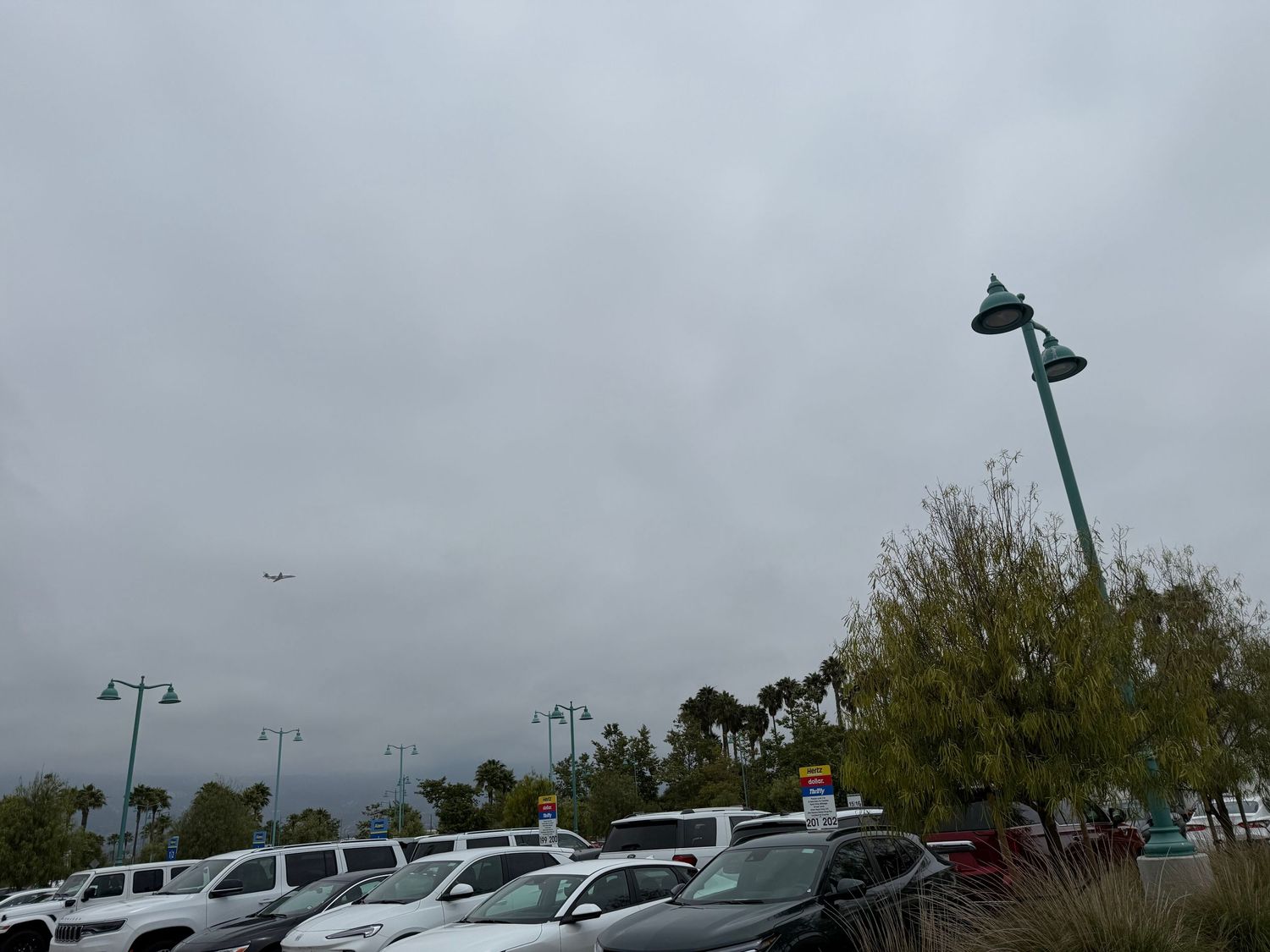 Aerial view of a parking lot filled with parked cars under cloudy skies at a commercial complex.