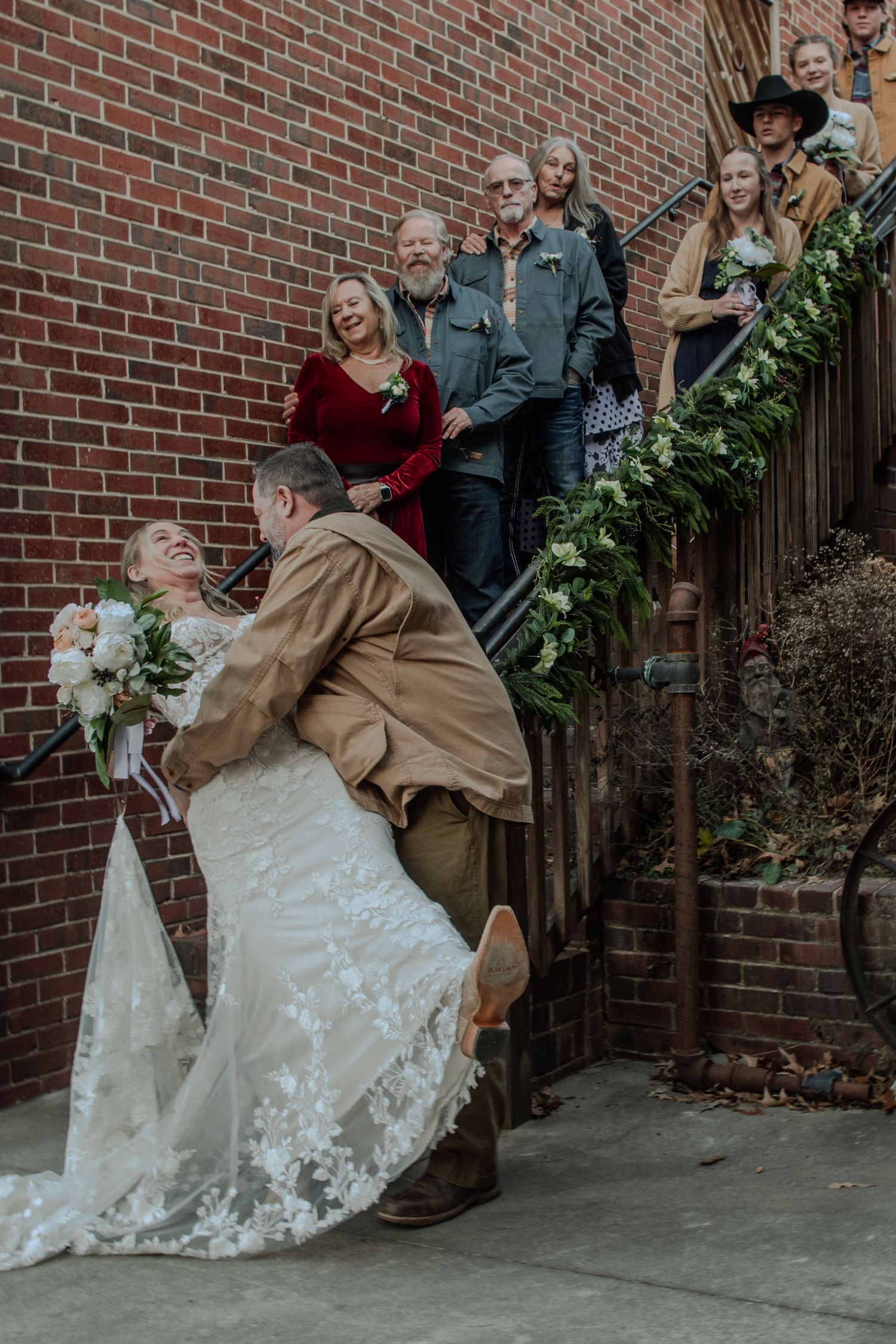 A sequence of images showing a bride being playfully dipped in front of a brick wall while wearing a lace wedding dress.