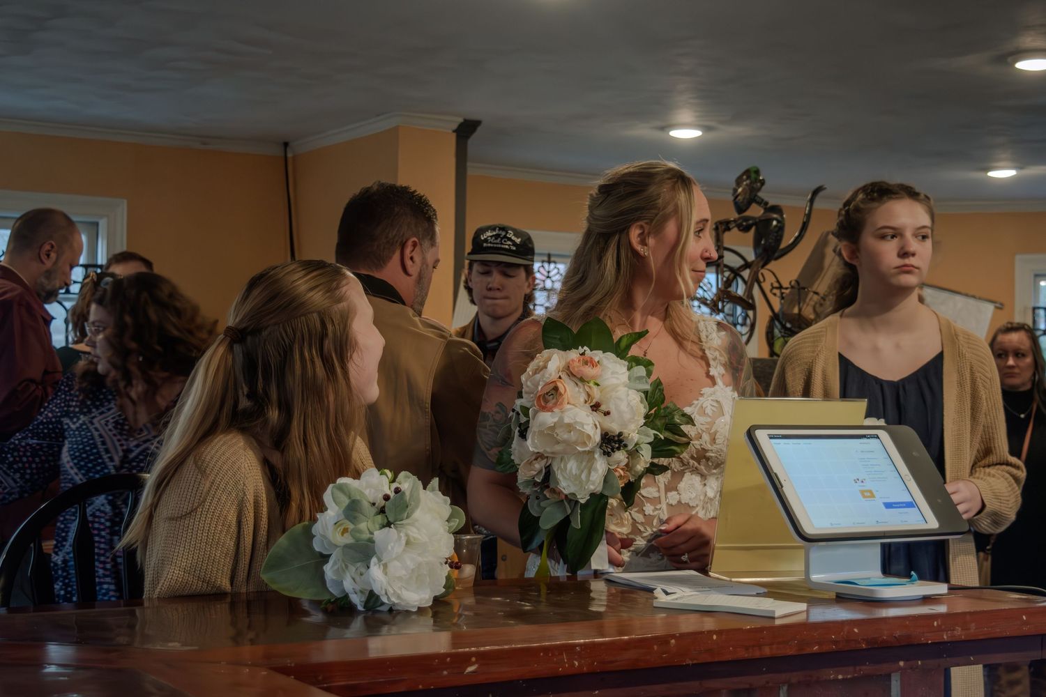 A group of people stand at a counter with bouquets of white flowers, interacting with a point-of-sale system.