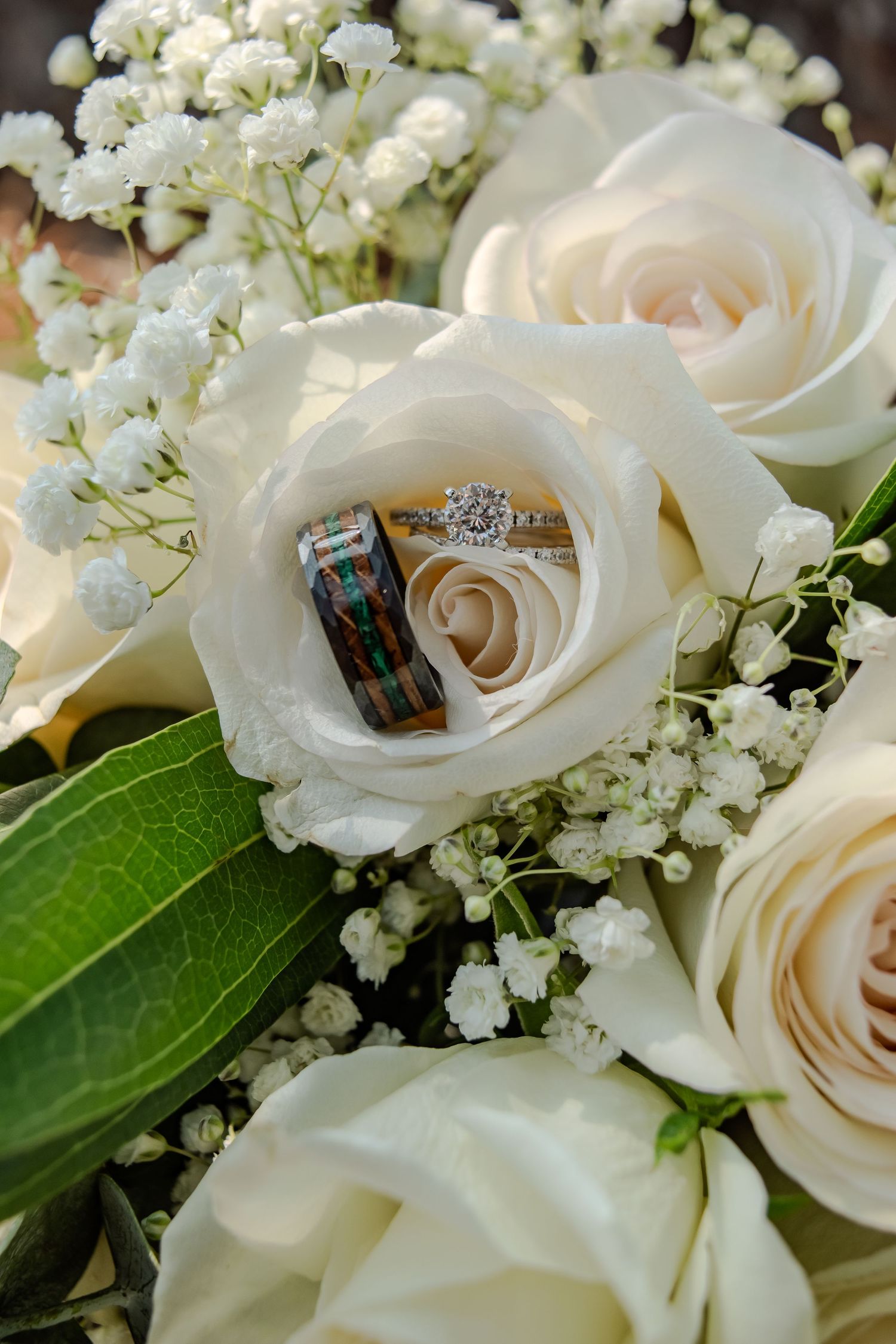 Wedding rings nestled inside white roses with baby's breath flowers and green foliage in an elegant bouquet.