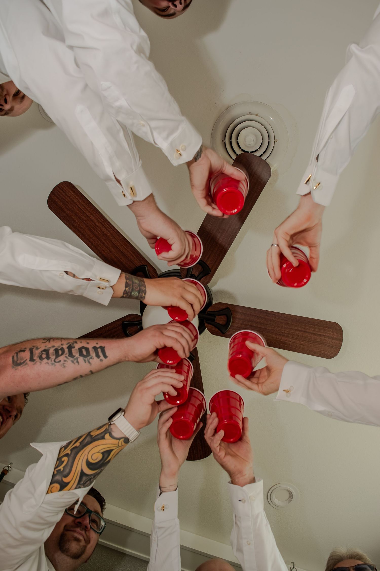 Several hands shown from above holding red cocktails in a celebratory toast while wearing white long-sleeved attire.