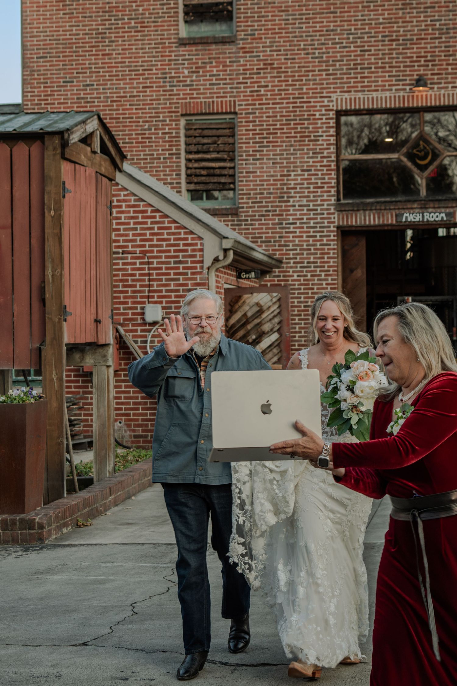 People interacting outdoors with a laptop in front of a brick building exterior.