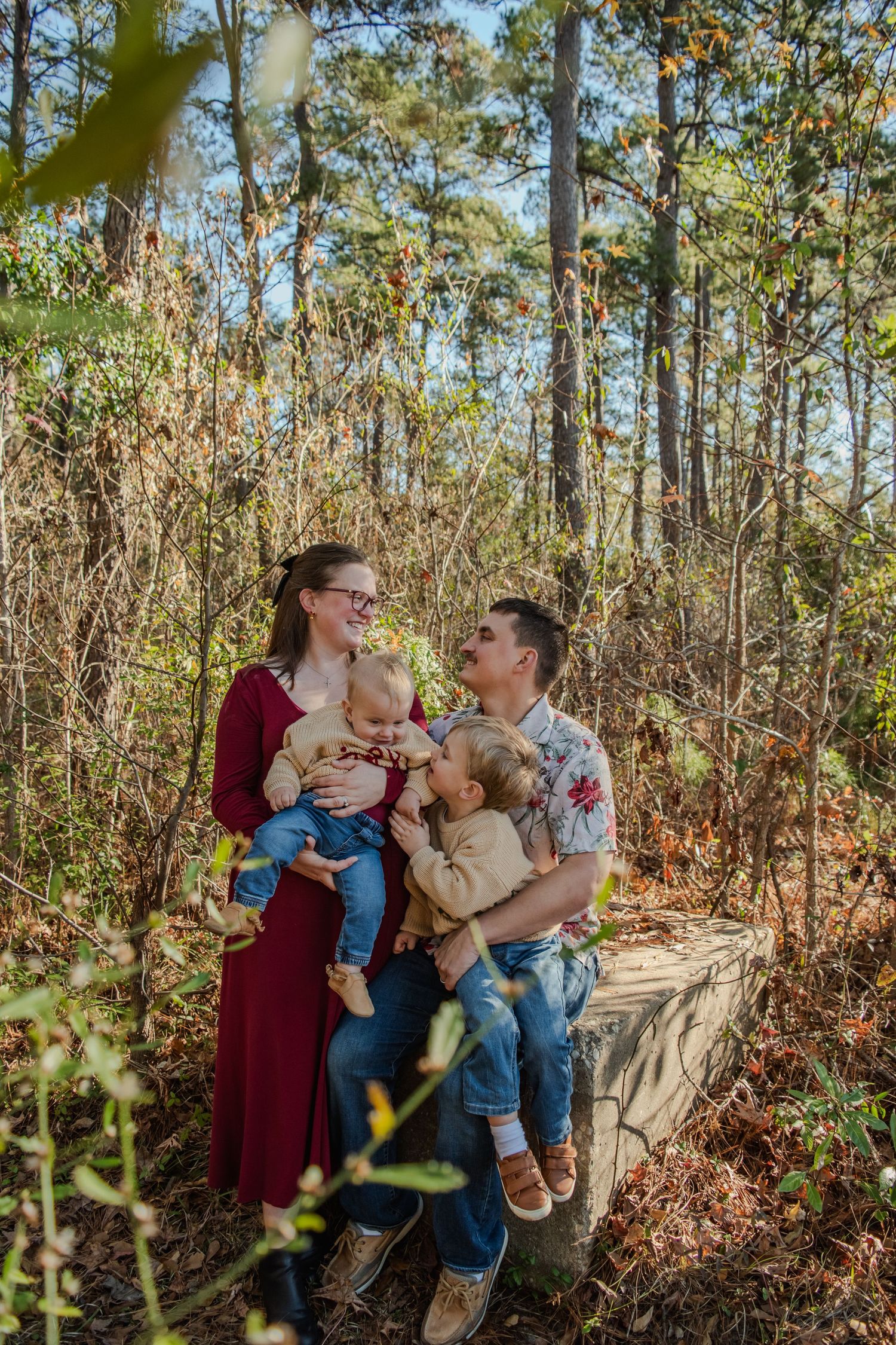 A family shares a joyful moment together while sitting on a fallen tree trunk in an autumn forest setting.