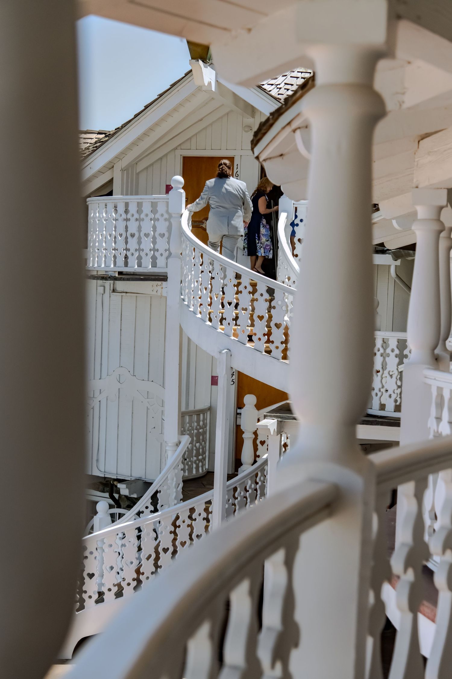 Elegant white spiral staircase with ornate railings on a historic building, with two people descending the steps.
