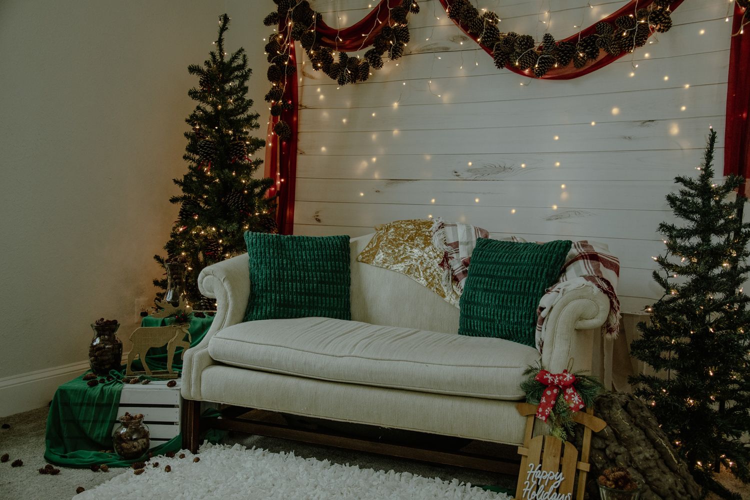 A cozy Christmas-themed photo studio setup with white furniture, garlands, and twinkling lights against a white backdrop.