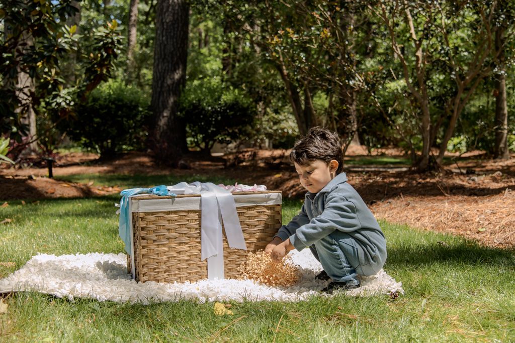 Young boy playing outdoors on a blanket beside a wicker basket in a lush green park setting.