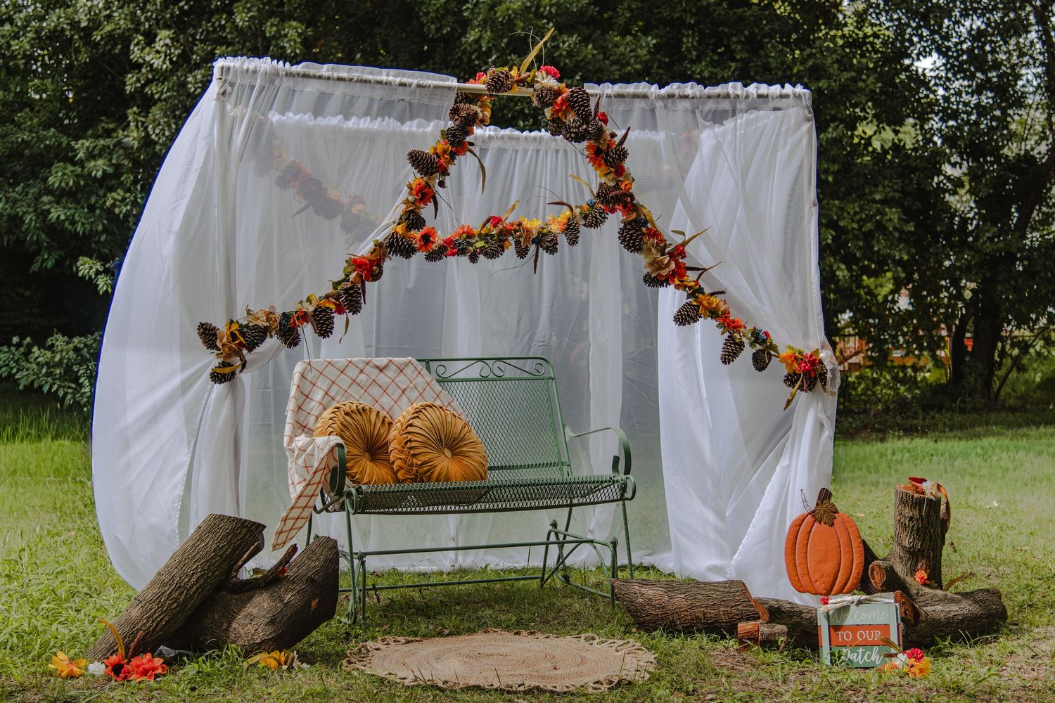 A row of fall decorations with pumpkins, orange garlands, benches, and white fabric draping in an outdoor setting.