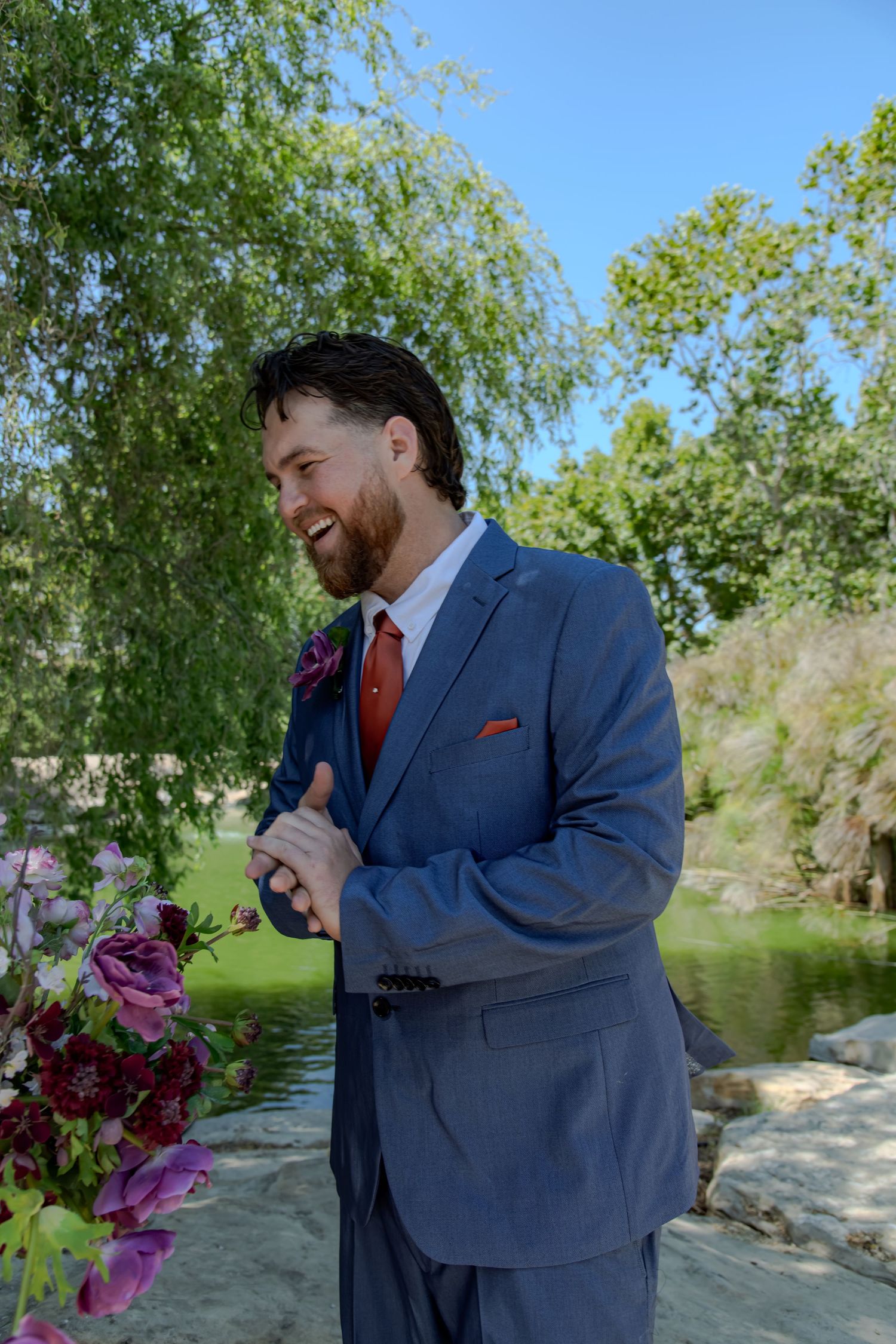 A couple shares an emotional moment during a wedding ceremony in a scenic outdoor setting with greenery.