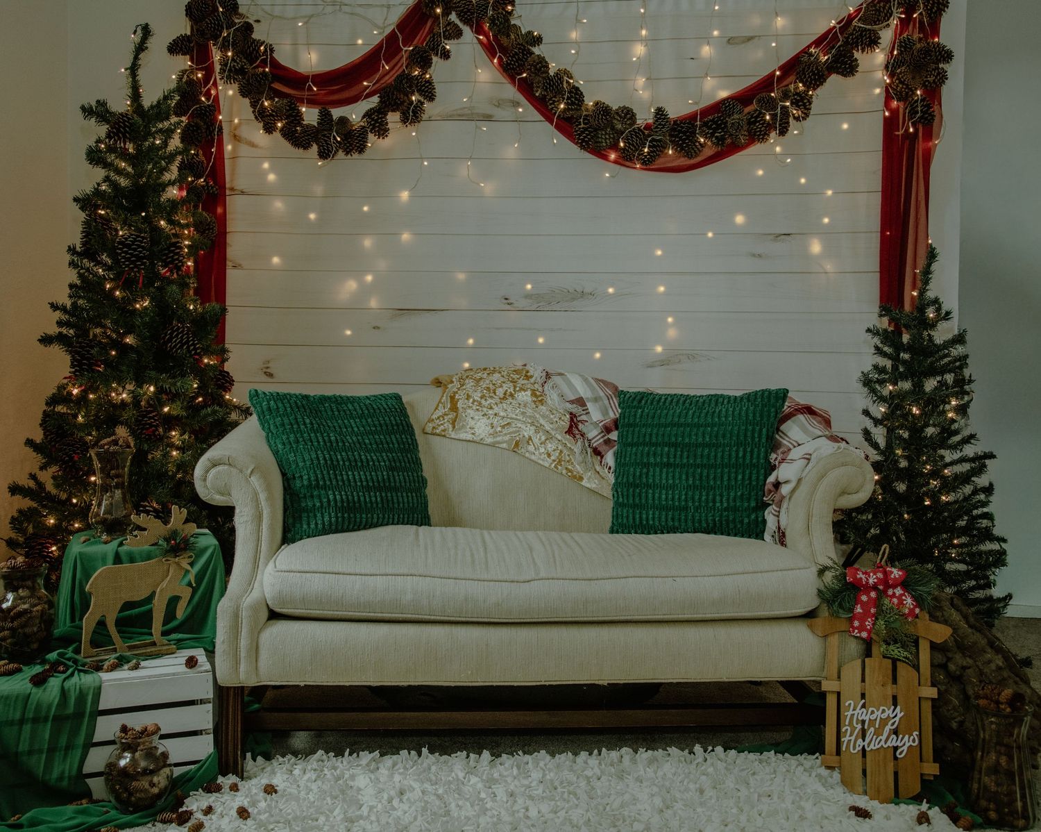 A cozy Christmas scene with a gray couch, emerald pillows, twinkling lights, and festive holiday garland decorations.