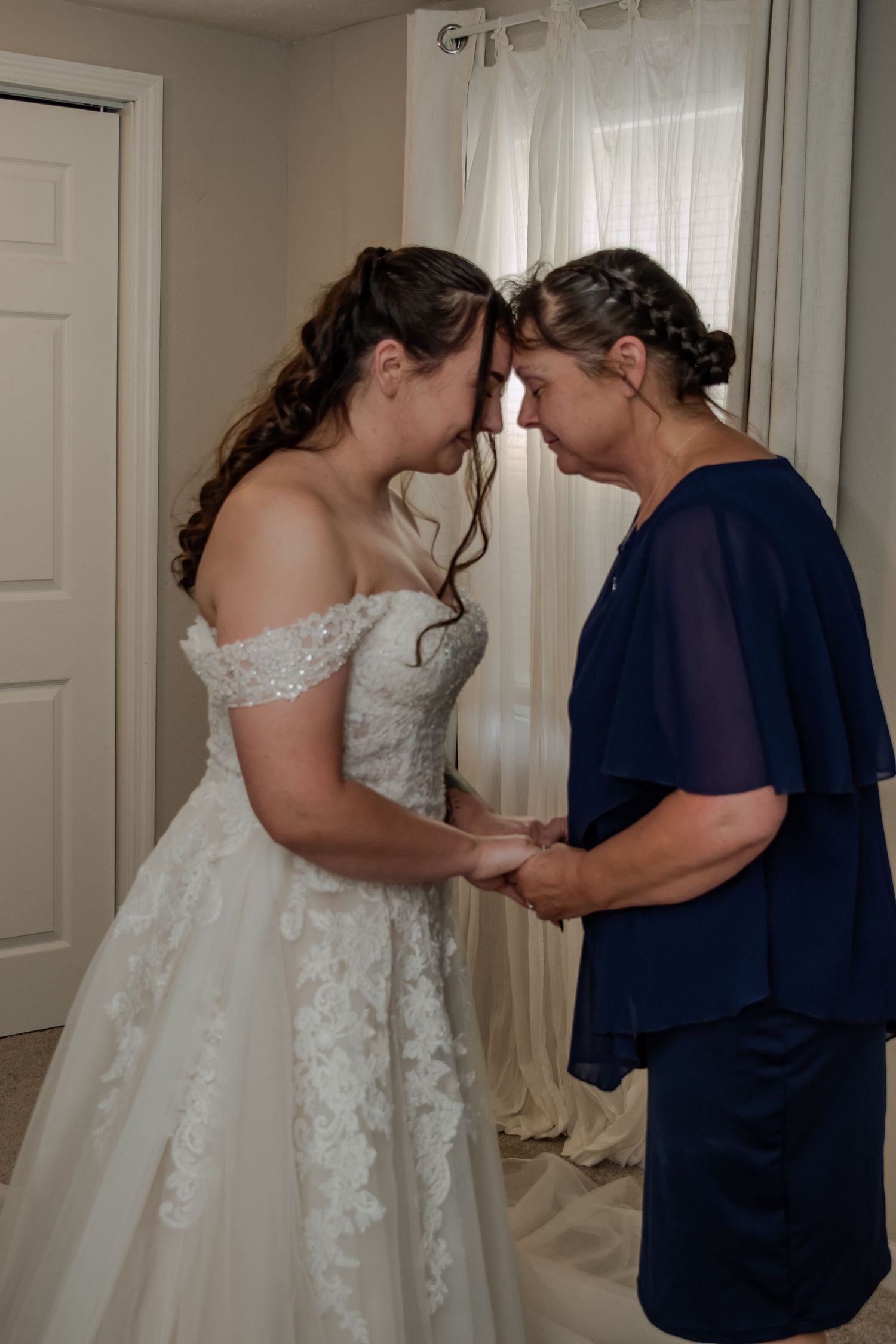 An intimate pre-wedding moment shows two people touching foreheads, with one wearing a lace wedding gown and the other in navy blue.