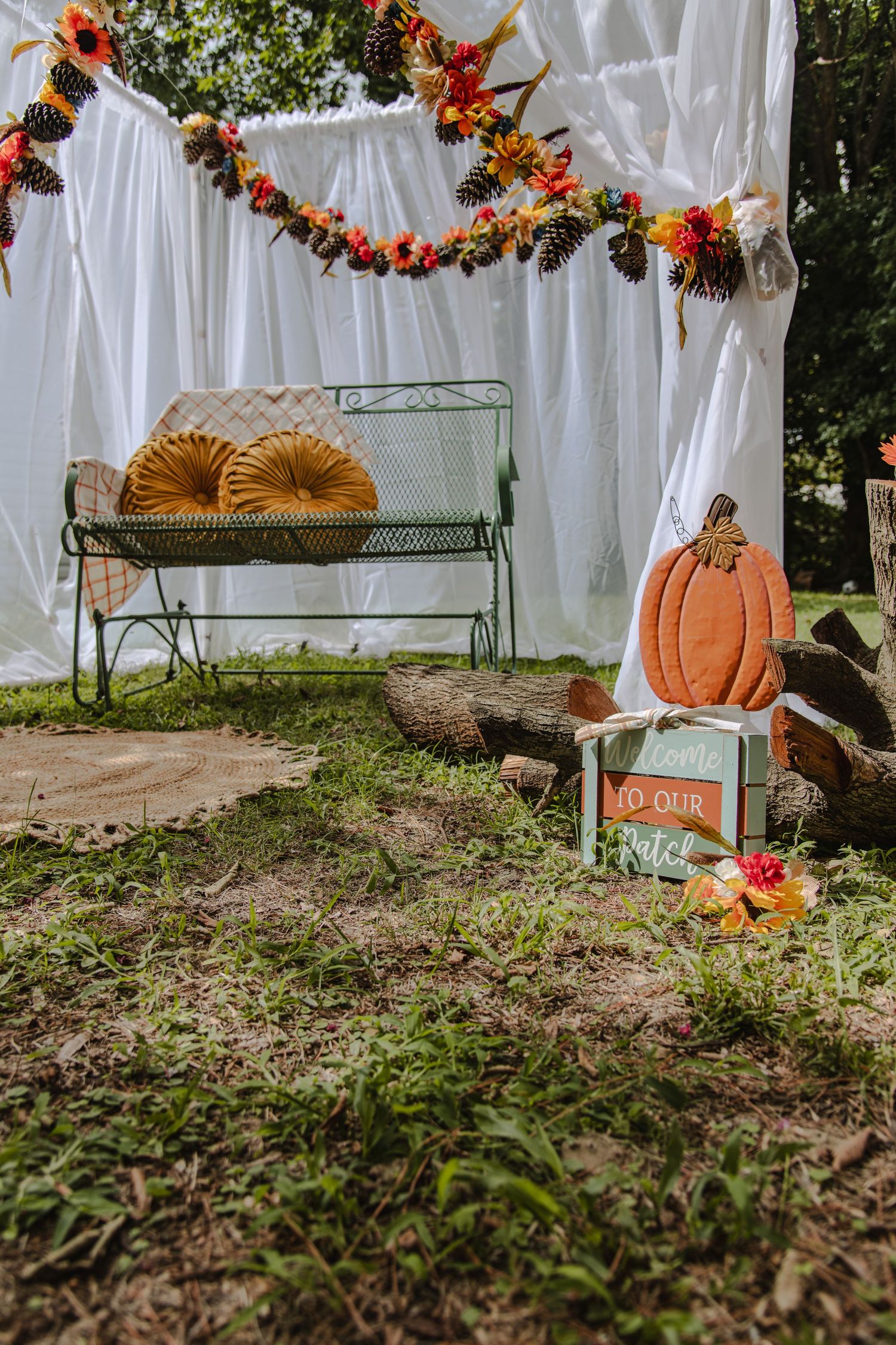 Fall outdoor photo setup with rustic bench, pumpkins, and autumn floral garland against white fabric backdrop.
