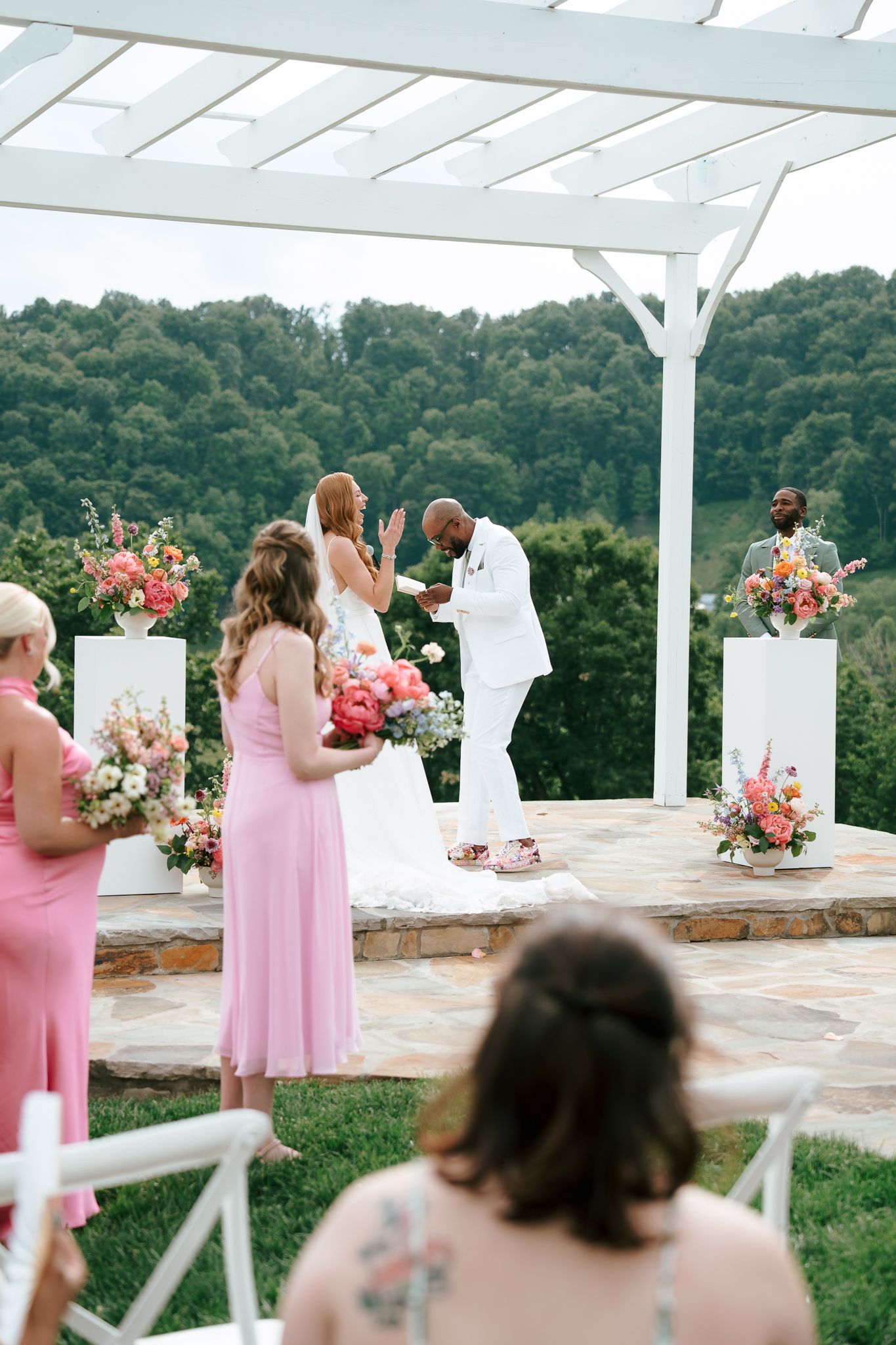 An outdoor wedding ceremony takes place under a white pergola with Booth Creative Co. NC Wedding Photographer