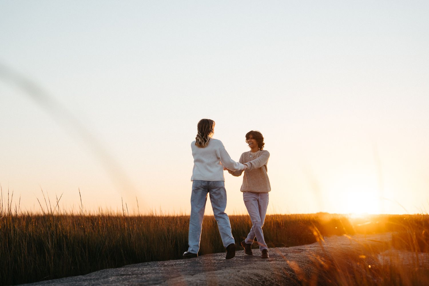 A Couple dances together on a grassy hill silhouetted against a golden sunset sky for their engagement photos with Booth Creative Co. ILM