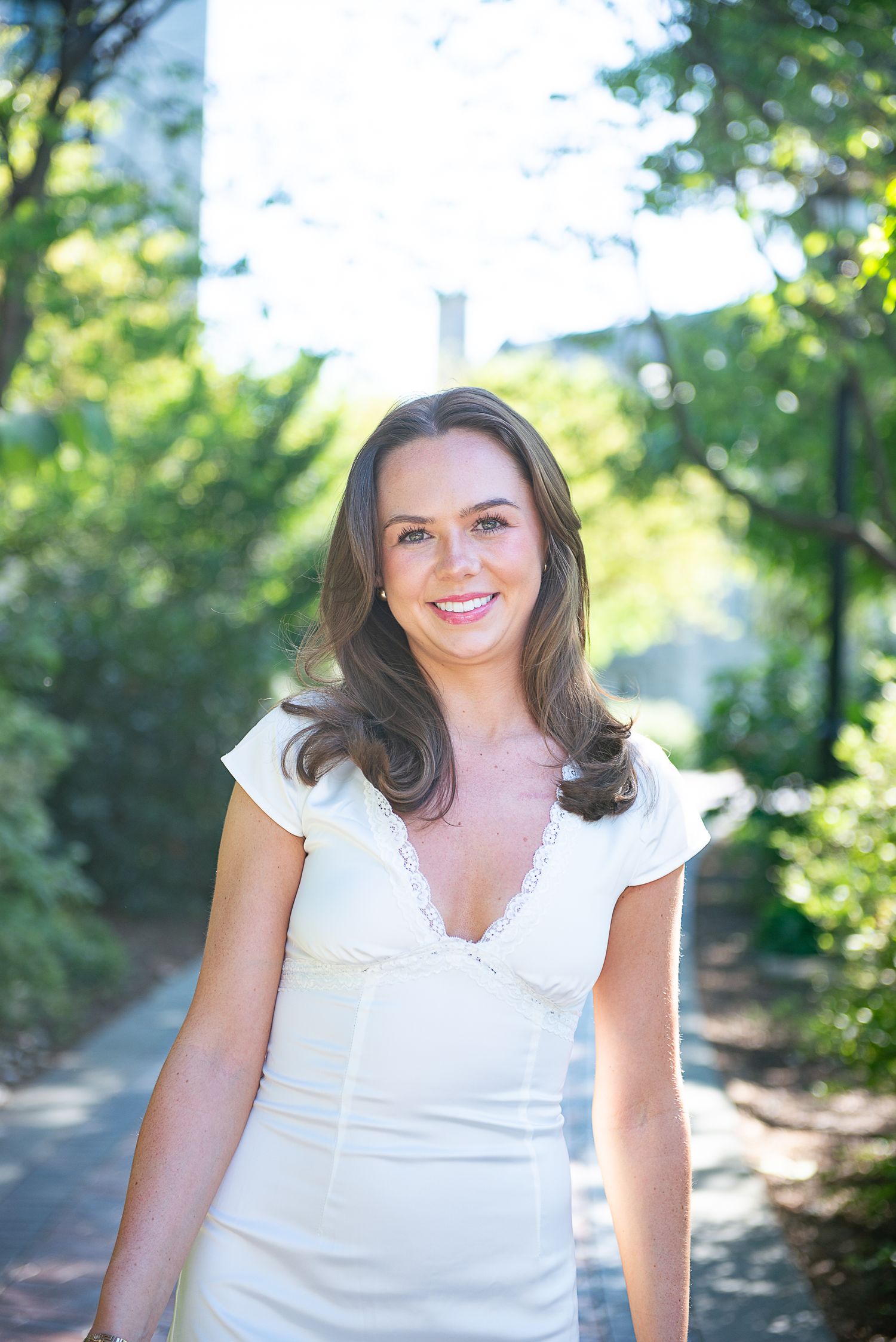 Graduation portrait in white summer dress against natural outdoor background.