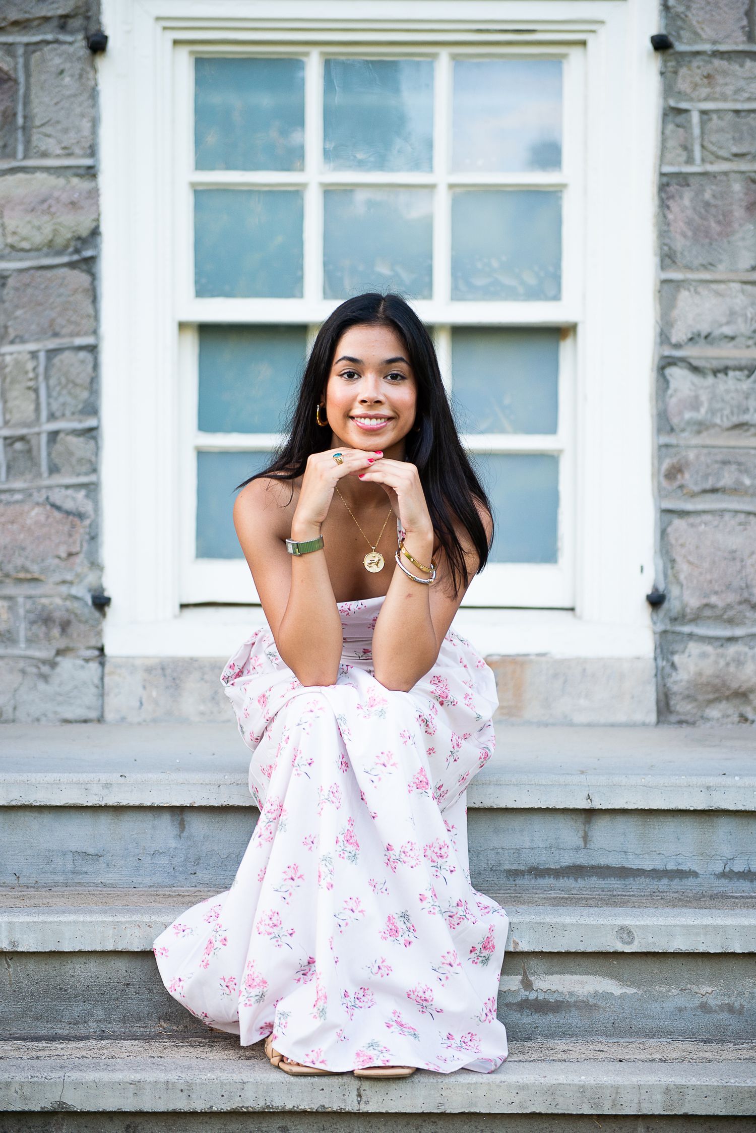 A senior in a floral dress creates an elegant scene against stone steps and a historic window backdrop.