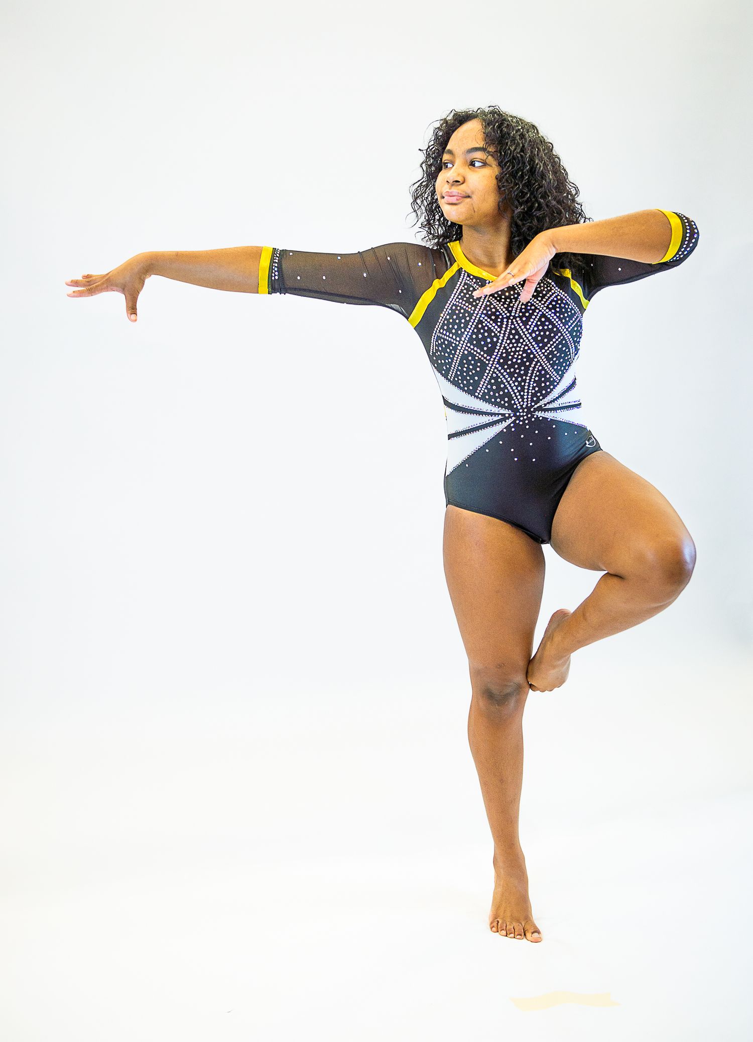 Gymnast in black and blue leotard striking an artistic pose against white background.
