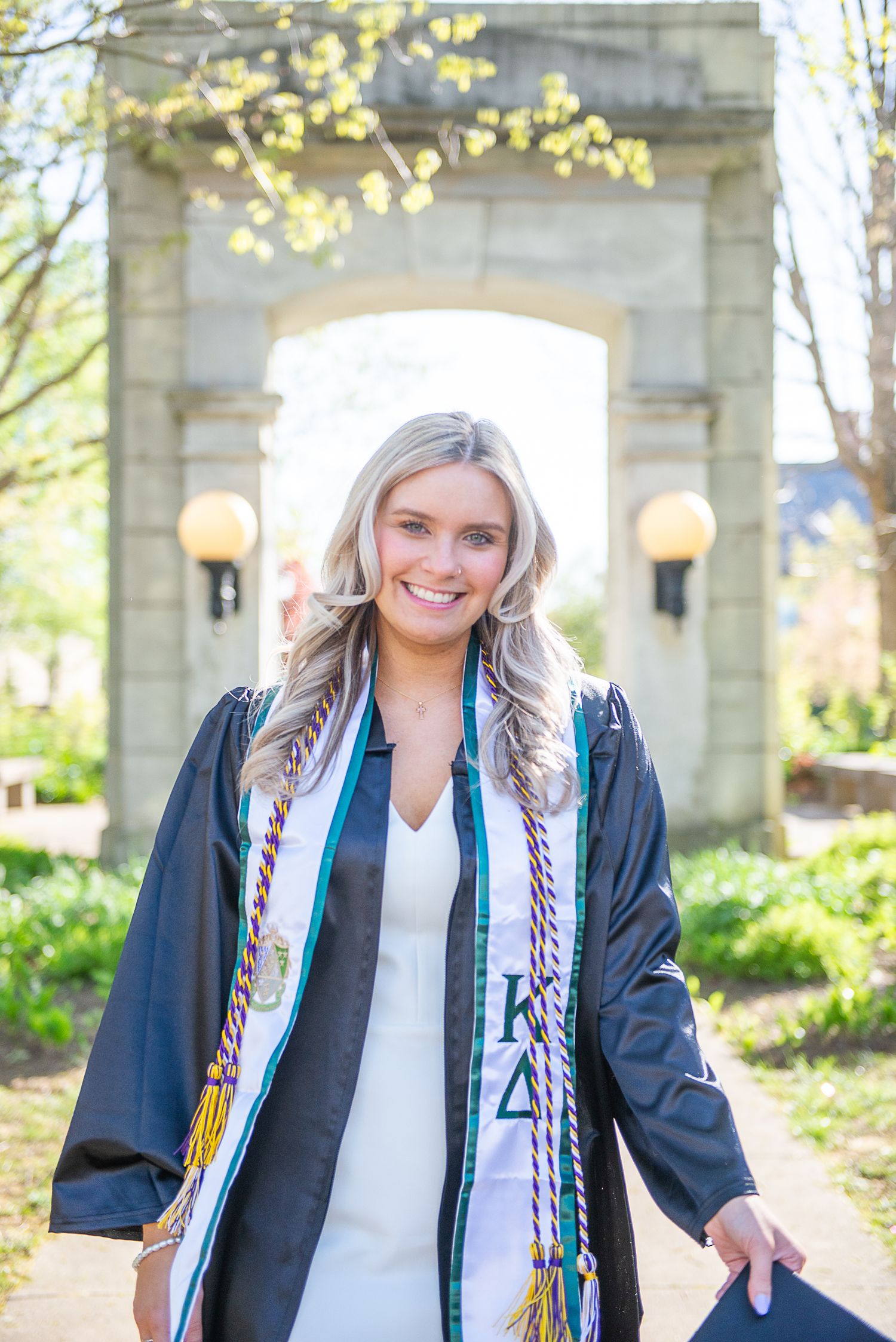 Graduate in academic regalia poses under stone archway on West Chester University's campus.
