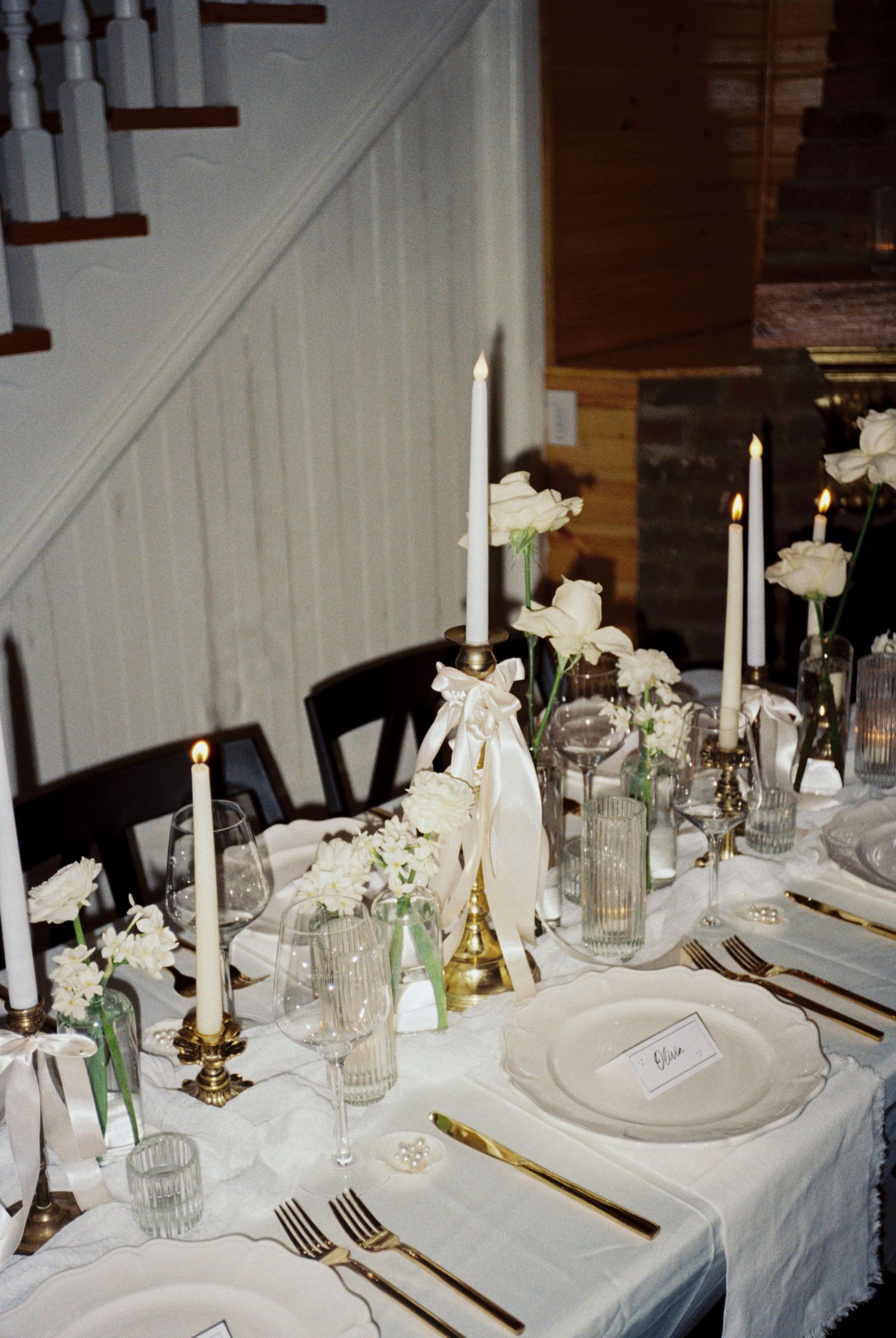 Elegant table setting with white flowers, taper candles and place settings arranged under a staircase.