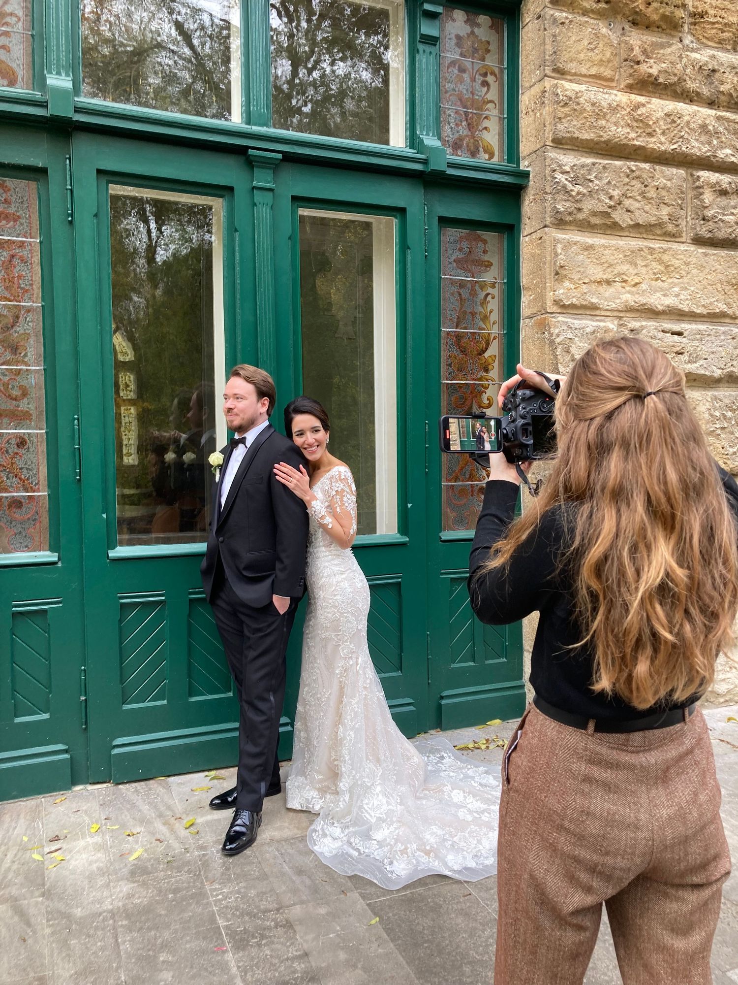 A photographer captures a couple posing in front of a historic building with green doors.