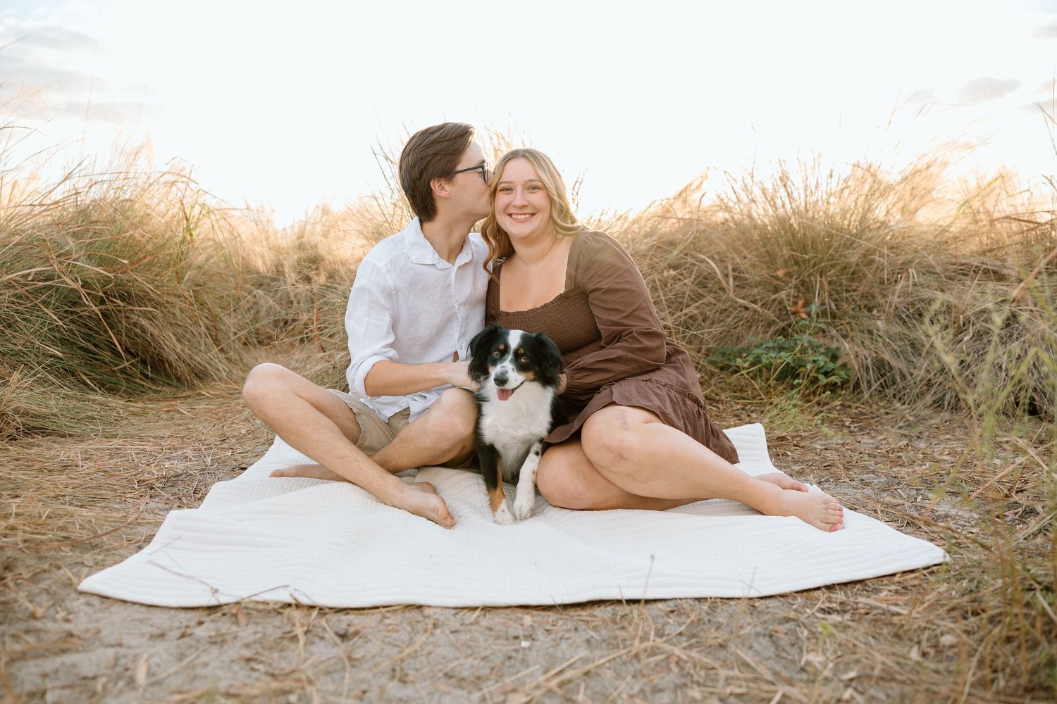 Couple sitting close together on a blanket in a grassy field during a couples photography session.