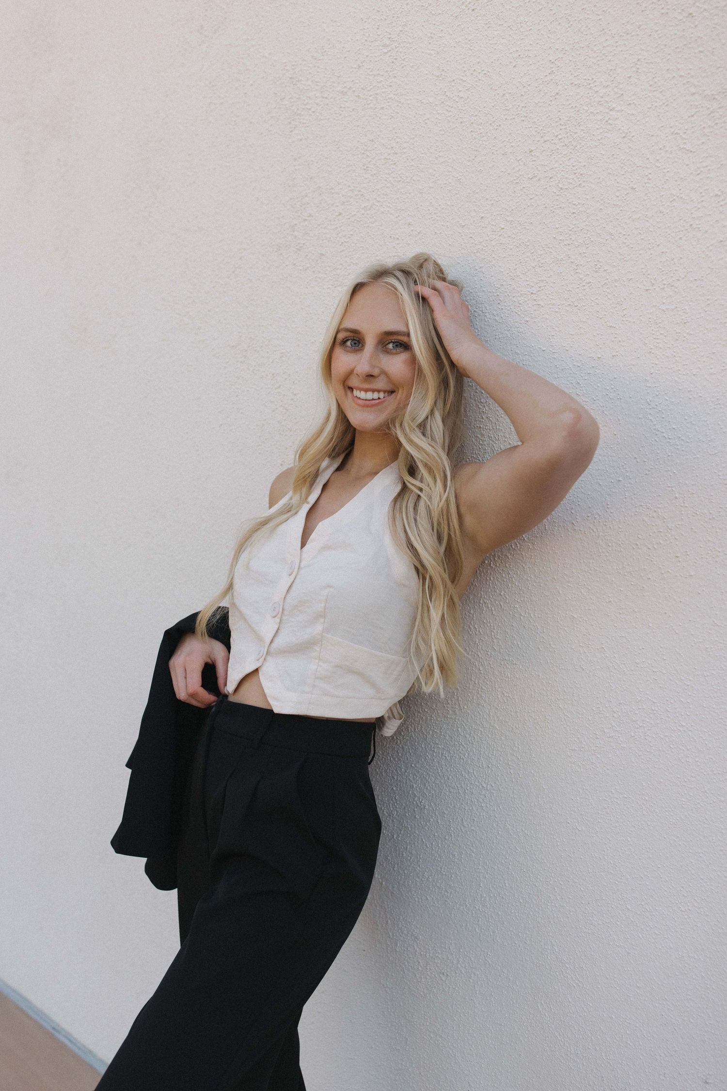Portrait of person in white top and black pants posing against white wall.