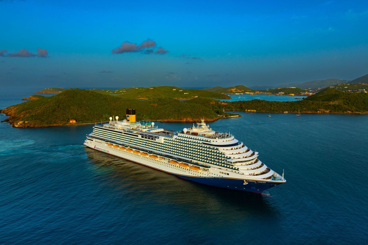 Aerial view of a luxury cruise ship sailing through turquoise Caribbean waters near tropical islands.