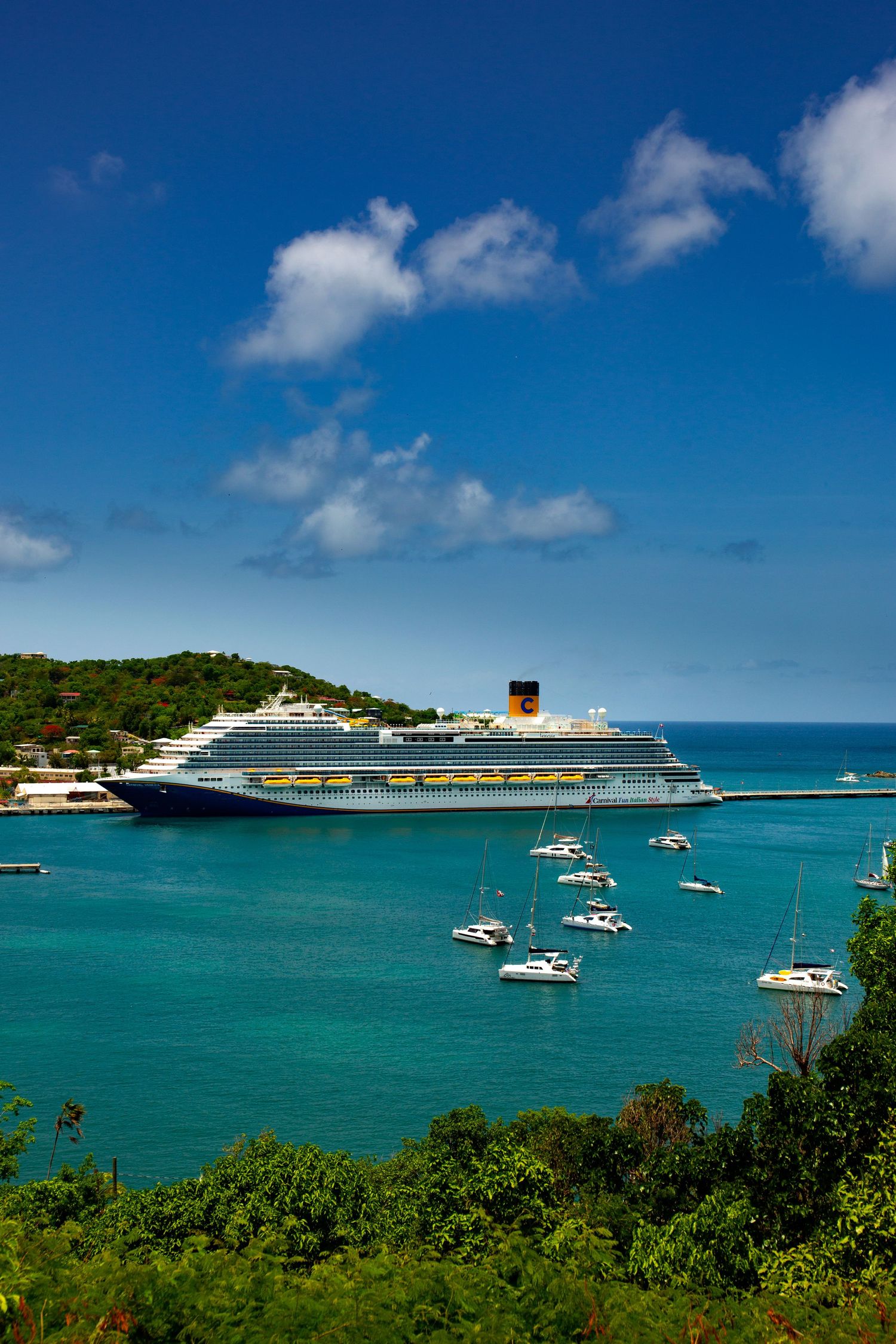 Large cruise ships and small boats anchored in turquoise Caribbean waters near a lush green tropical island under blue skies.