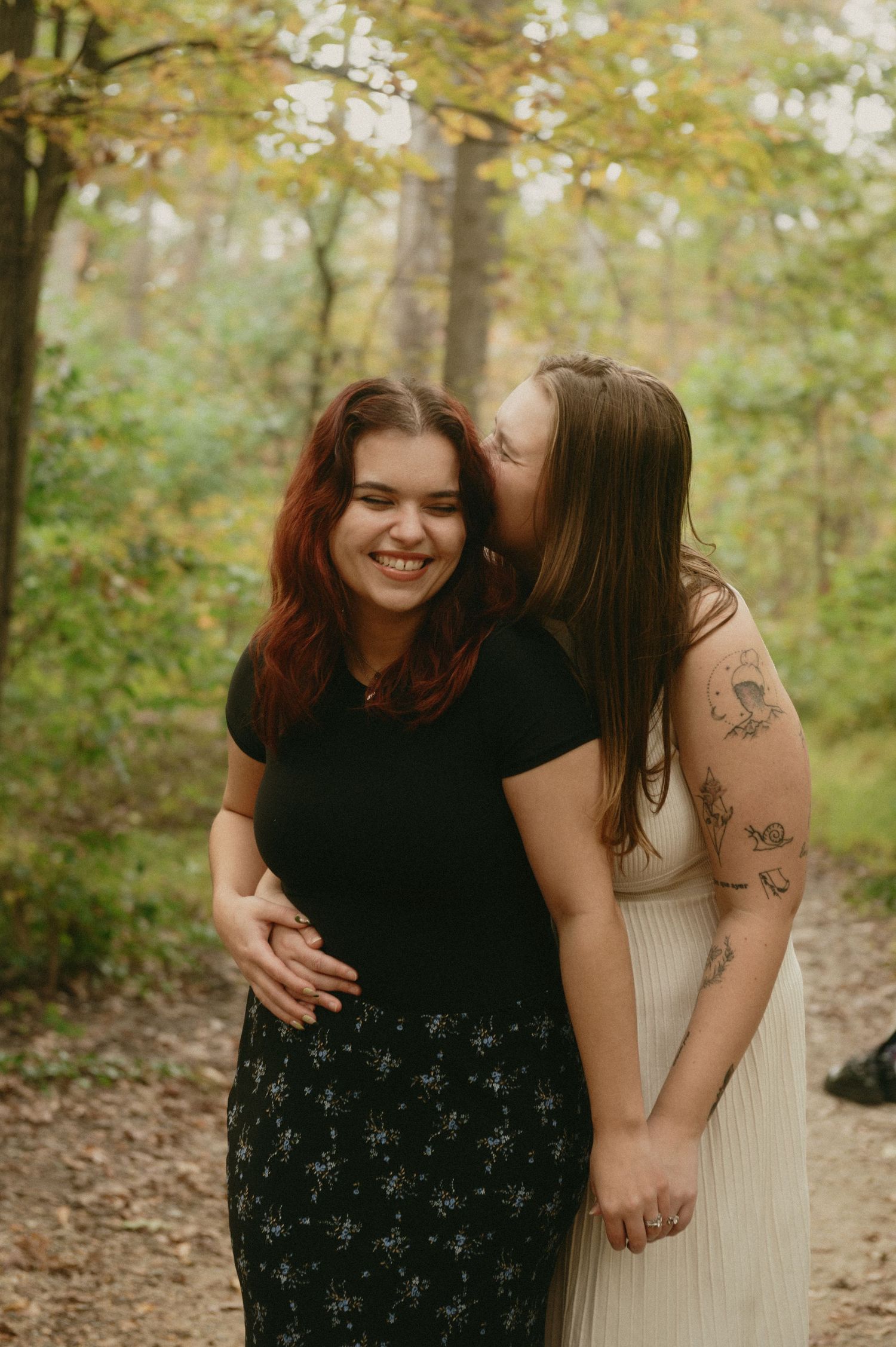 Two people share a tender moment together while standing on a leaf-covered forest path in autumn.