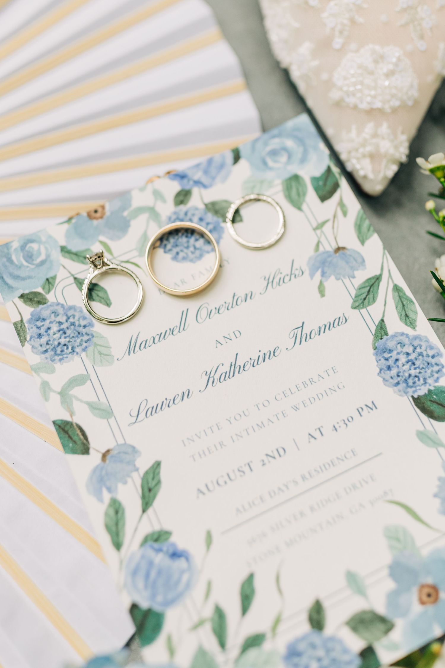 Elegant wedding invitation with blue floral design, gold wedding bands, and diamond ring for Maxwell and Lauren's August ceremony.