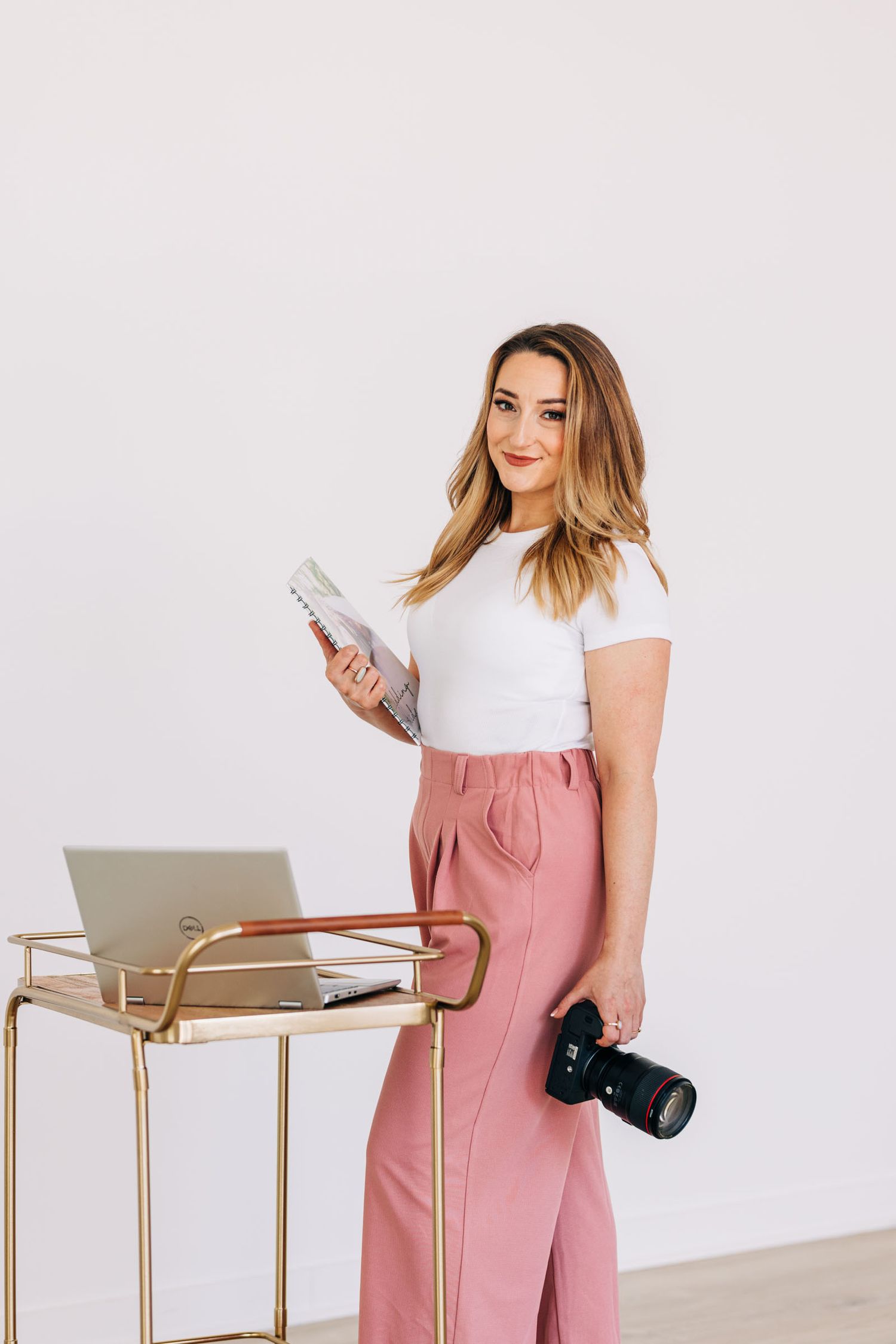 Professional photographer standing by desk with camera and papers in casual business attire.