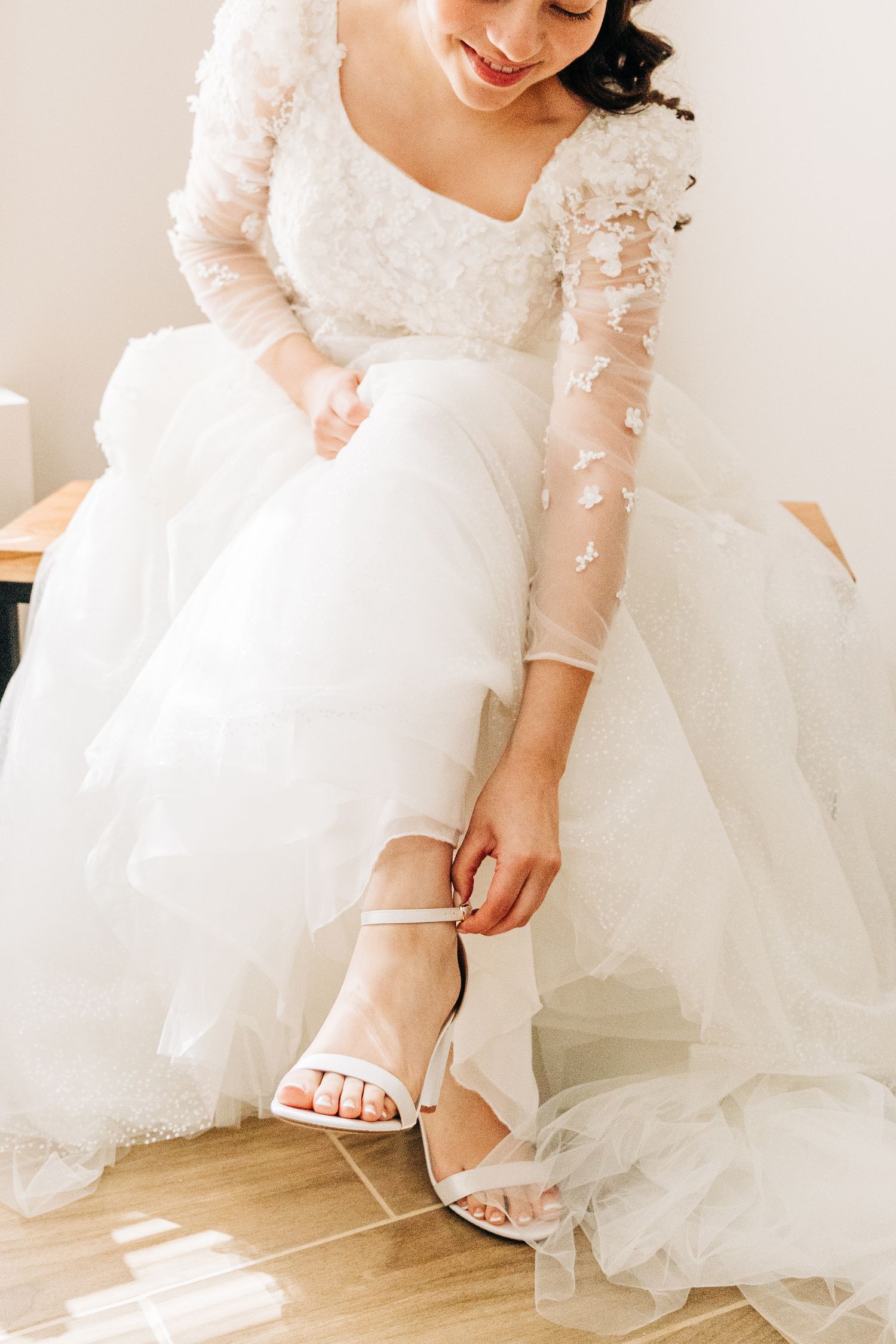 Bride in lace long sleeve wedding dress adjusting white sandal strap.